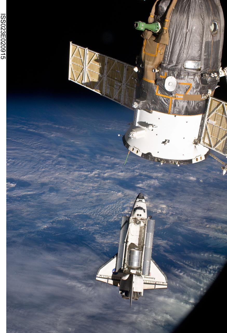 ISS023-E-020915 (7 April 2010) --- The space shuttle Discovery and the International Space Station are in the midst of their rendezvous and docking activities in this image photographed by an Expedition 23 crew member aboard the orbital outpost. Part of a docked Russian spacecraft can be seen in the foreground.