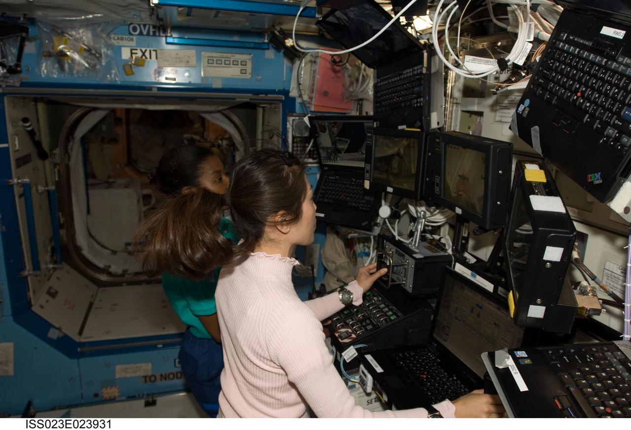 ISS023-E-023931 (15 April 2010) --- Japan Aerospace Exploration Agency astronaut Naoko Yamazaki and NASA astronaut Stephanie Wilson (partially obscured), both STS-131 mission specialists, work at a robotic workstation in the Destiny laboratory of the International Space Station while space shuttle Discovery remains docked with the station.