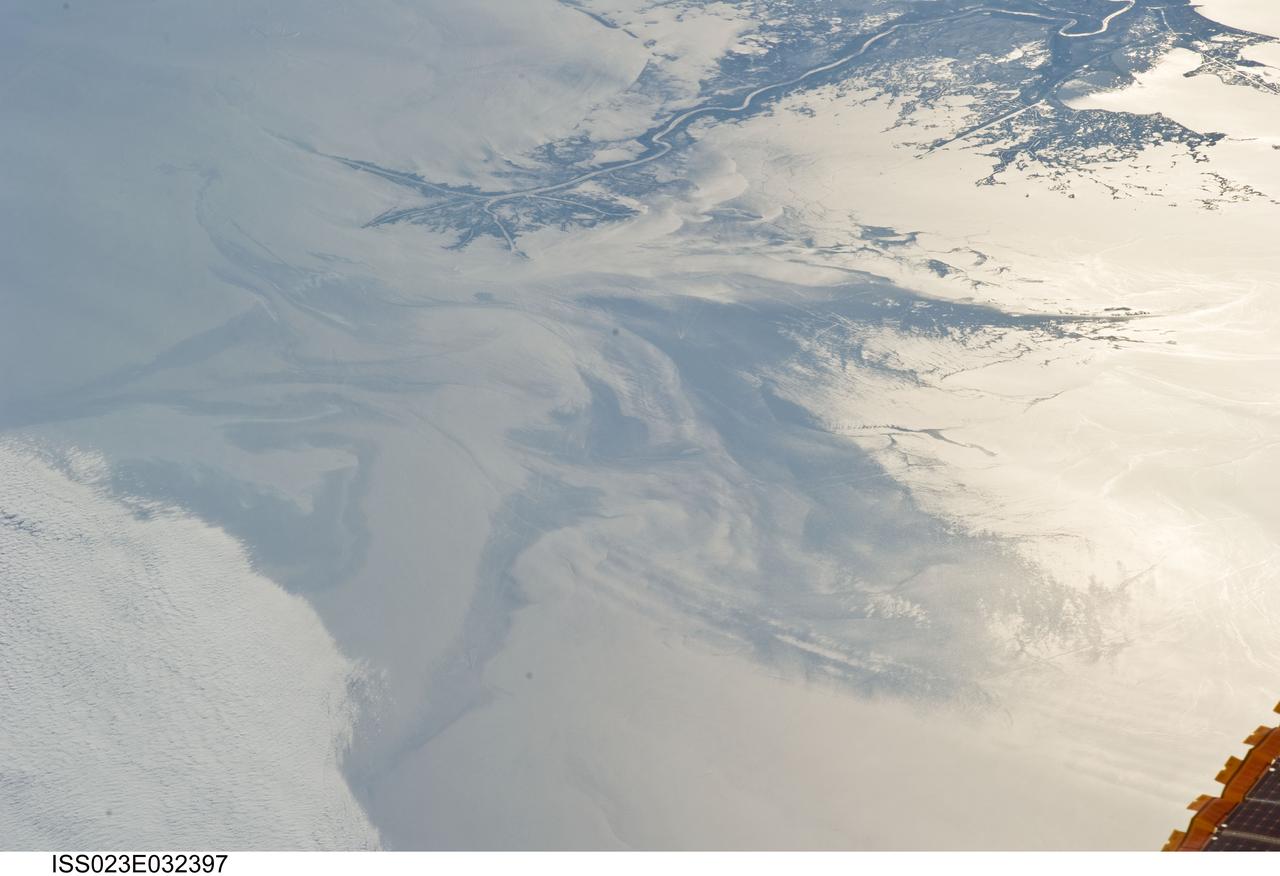ISS023-E-032397 (4 May 2010) --- The Gulf of Mexico oil spill is featured in this image photographed by an Expedition 23 crew member on the International Space Station. On April 20, 2010 the oil rig Deepwater Horizon suffered an explosion and sank two days later. Shortly thereafter oil began leaking into the Gulf of Mexico from ruptured pipes as safety cutoff mechanisms failed to operate. Automated nadir-viewing orbital NASA sensors have been tracking the growth of the oil spill as it has spread towards the northern Gulf Coast. This detailed photograph provides a different viewing perspective on the ongoing event. The image is oblique, meaning that it was taken with a sideways viewing angle from the space station, rather than the ?straight down? or nadir view typical of automated satellite sensors. The view is towards the west; the ISS was located over the eastern edge of the Gulf of Mexico when the image was taken. The Mississippi River Delta and nearby Louisiana coast (top) appear dark in the sunglint that illuminates most of the image. This phenomenon is caused by sunlight reflecting off the water surface ? much like a mirror ? directly back towards the astronaut observer onboard the orbital complex. The sunglint improves the identification of the oil spill (colored dark to light gray) which is creating a different water texture, and therefore a contrast, between the smooth and rougher water of the reflective ocean surface (colored silver to white).  Wind and water current patterns have modified the oil spill?s original shape into streamers and elongated masses. Efforts are ongoing to contain the spill and protect fragile coastal ecosystems and habitats such as the Chandeleur Islands (right center). Other features visible in the image include a solid field of low cloud cover at the lower left corner of the image. A part of one of the ISS solar arrays is visible at lower right. Wave patterns at lower right are most likely caused by tidal effects.