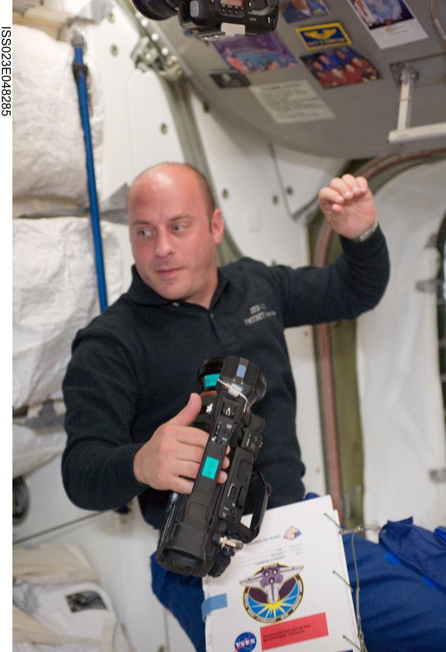 ISS023-E-048285 (19 May 2010) --- NASA astronaut Garrett Reisman, STS-132 mission specialist, holds a High Definition Video (HDV) camera in the Unity node of the International Space Station while space shuttle Atlantis remains docked with the station.