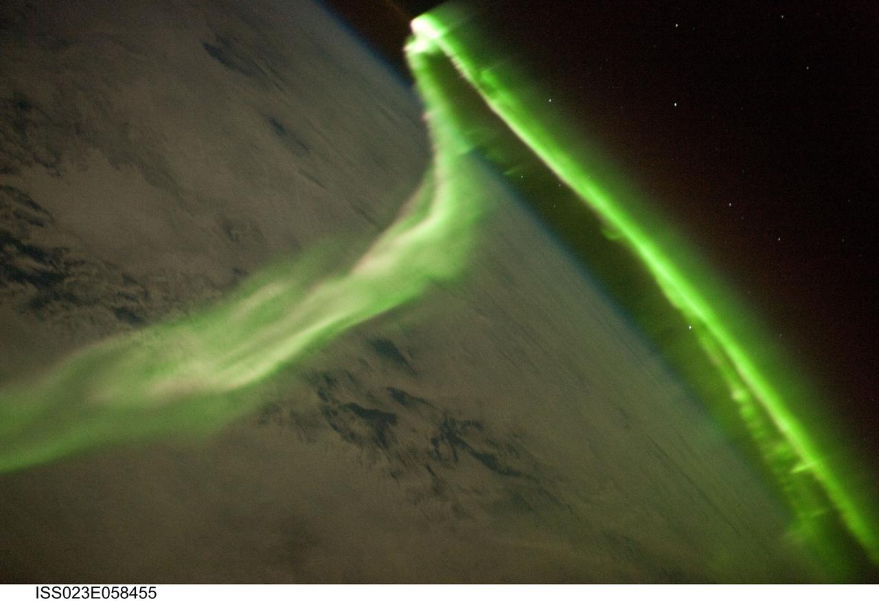 ISS023-E-058455 (29 May 2010) --- Aurora Australis is featured in this image photographed by an Expedition 23 crew member on the International Space Station. Among the views of Earth afforded crew members aboard the ISS, surely one of the most spectacular is of the aurora. These ever-shifting displays of colored ribbons, curtains, rays, and spots are most visible near the North (Aurora Borealis) and South (Aurora Australis) Poles as charged particles streaming from the sun (the solar wind) interact with Earth’s magnetic field, resulting in collisions with atoms of oxygen and nitrogen in the upper atmosphere. The atoms are excited by these collisions, and typically emit photons as a means of returning to their original energy state. The photons form the aurora that we see. The most commonly observed color of aurora is green, caused by photons (light) emitted by excited oxygen atoms at wavelengths centered at 0.558 micrometers, or millionths of a meter. Visible light is reflected from healthy (green) plant leaves at approximately the same wavelength. Red auroras are generated by light emitted at a longer wavelength (0.630 micrometers), and other colors such as blue and purple are also sometimes observed. While auroras are generally only visible close to the poles, severe magnetic storms impacting Earth’s magnetic field can shift them towards the equator. This striking aurora image was taken during a geomagnetic storm that was most likely caused by a coronal mass ejection from the sun on May 24, 2010. The ISS was located over the Southern Indian Ocean at an altitude of 350 kilometers, with the observer most likely looking towards Antarctica (not visible) and the South Pole. The aurora has a sinuous ribbon shape that separates into discrete spots near the lower right corner of the image. While the dominant coloration of the aurora is green, there are faint suggestions of red photon emission as well (light fuscia tones at center left). Dense cloud cover is dimly visible below the aurora. The curvature of Earth’s horizon, or limb, is clearly visible as is the faint blue line of the upper atmosphere directly above at top center. Several stars appear as bright pinpoints against the blackness of space at top right.