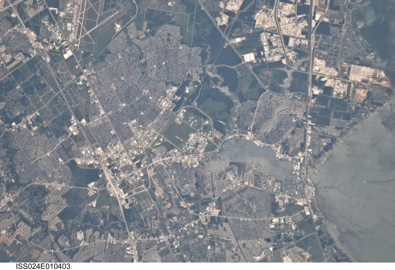 ISS024-E-010403 (31 July 2010) --- This detailed image ? photographed by an Expedition 24 crew member on the International Space Station (ISS) ? is centered on the NASA Lyndon B. Johnson Space Center (JSC), located in the southeastern Houston, TX metropolitan area. While initially being represented by a number of temporary locations in Houston, the facility was established in 1961 as the Manned Spacecraft Center and renamed in honor of the late U.S. President Johnson (a Texas native) in 1973. JSC serves as the lead NASA center for both astronaut training and mission control of manned spacecraft - such as the ISS and space shuttle - and has done so throughout the history of the U.S. manned space program. The Center also collaborates with other NASA and international partner facilities in a variety of scientific and engineering programs related to human spaceflight and planetary exploration. JSC is located approximately midway between downtown Houston and Galveston, TX, and is bordered by several smaller municipalities that form a mosaic of urban and suburban land use (grey areas with street grids, and commercial/industrial areas characterized by white rooftops). Large tracts of grassy fields and forests in the area (light to dark green respectively) include nature preserves, grazing lands, and flood control areas. Also visible at upper left is Ellington Field. This airport services a variety of NASA aircraft used for astronaut training, scientific, and cargo transport purposes. Clear Lake, an inlet of Galveston Bay, is located to the immediate southeast of JSC. Both Clear Lake and Galveston Bay appear silver-grey due to sunglint, or light reflected back towards the observer on the ISS that gives the water surface a mirror-like appearance. Several boat wakes are visible in Galveston Bay (right) due to disruption of the water surface that reduces the sunglint effect.