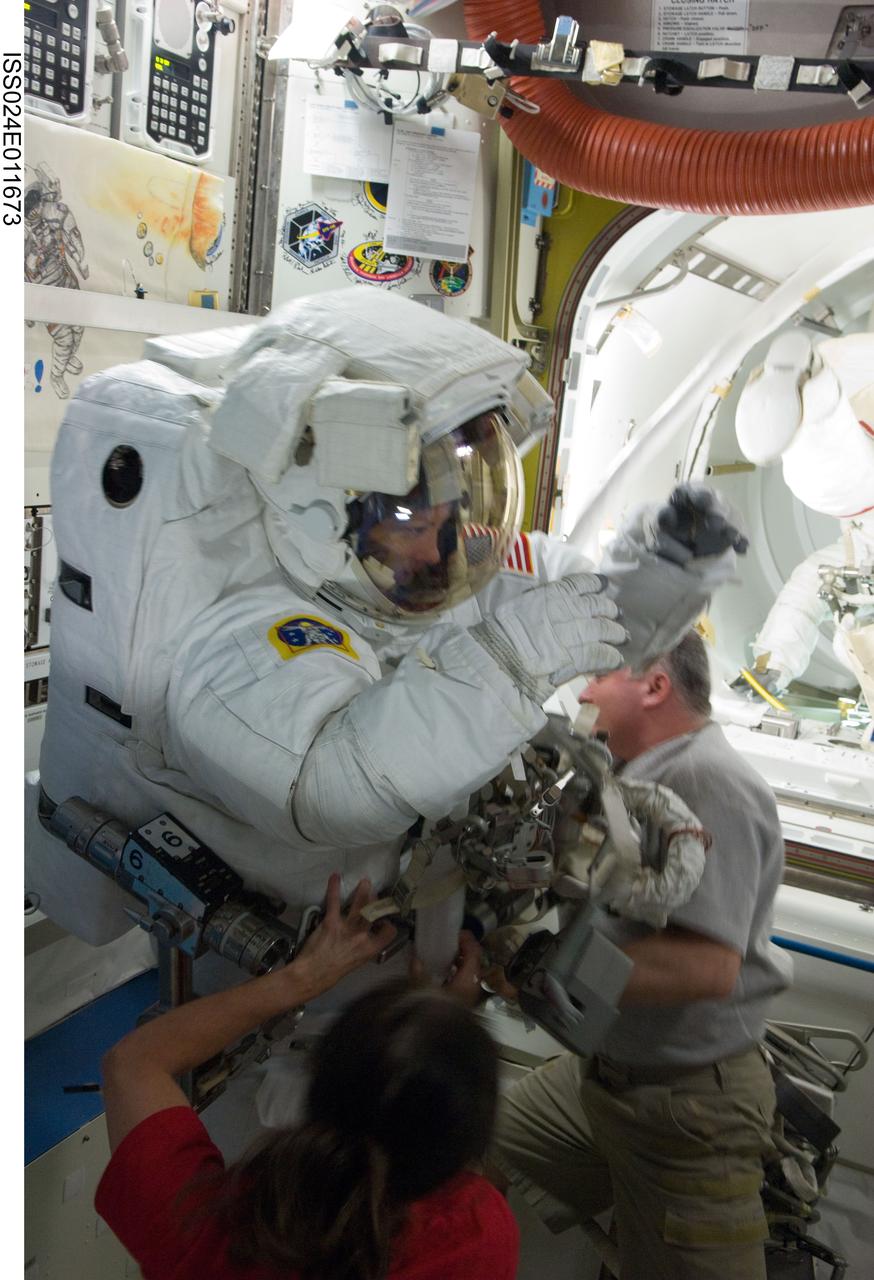 ISS024-E-011673 (11 Aug. 2010) --- NASA astronaut Tracy Caldwell Dyson, Expedition 24 flight engineer, attired in her Extravehicular Mobility Unit (EMU) spacesuit, is pictured in the Quest airlock of the International Space Station as the second of three planned spacewalks to remove and replace an ammonia pump module that failed July 31 draws to a close. NASA astronaut Shannon Walker and Russian cosmonaut Fyodor Yurchikhin, both flight engineers, assist Caldwell Dyson with the doffing of her spacesuit.