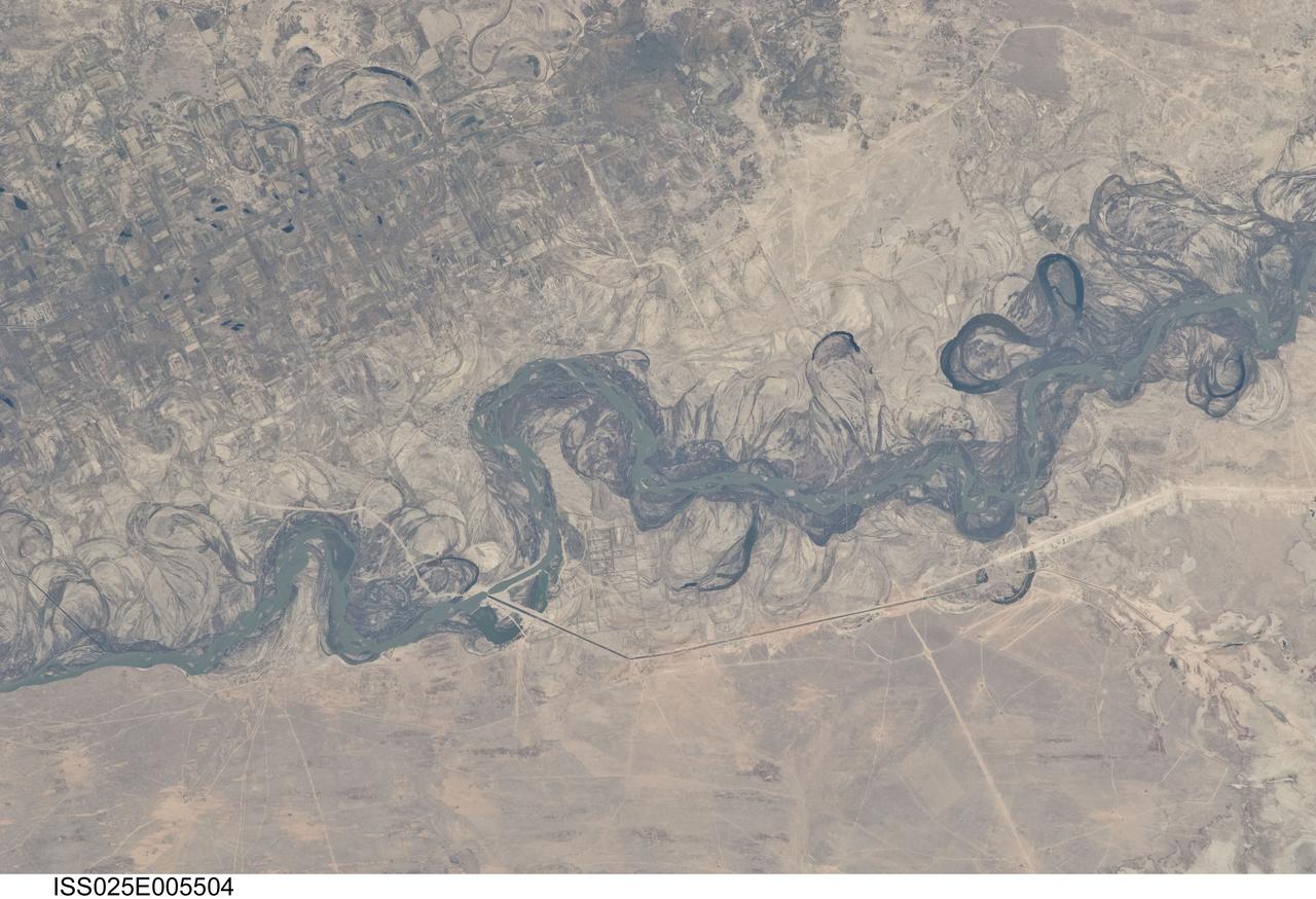 ISS025-E-005504 (30 Sept. 2010) --- Syr Dar’ya River floodplain in Kazakhstan, central Asia is featured in this image photographed by an Expedition 25 crew member on the International Space Station. Central Asia’s most important cotton-growing region is concentrated in the floodplain of the Syr Dar’ya, and is irrigated by water from the river. The floodplain is shown here as a tangle of twisting meanders and loops (center). The darkest areas are brushy vegetation along the present course (filled with blue-green water); wisps of vegetation are also visible along flanking swampy depressions, or sloughs. An older floodplain appears as an area of more diffuse dark vegetation (upper left), where a pattern of relict meander bends is overlain by a rectangular pattern of cotton fields. The straight channel of a new diversion canal—one of sixteen from this point downstream—can be seen along the east bank of the river. The older floodplain area is fed from the Chardara Reservoir immediately upstream (not shown). Half the river flow is controlled from reservoirs, and half from direct water take-off from canals. By contrast with the intensive agricultural use of water shown here, upstream water control in the mountain valleys is oriented more toward power generation. The river flows for a total distance of 2,200 kilometers from the Tien Shan Mountains westward and northwestward to the Aral Sea—the dying waterbody at the low point of the basin far to the northwest. Withdrawals of water from the river for agriculture have continued for many decades. Although the Syr Dar’ya is the second largest river flowing into the sea, its discharge is not very large. As such, it has been easily depleted, with none of its water today reaching the Aral Sea. Control of the river is vested in the Syr Dar’ya Basin Water Organization run by nations with territory in the Syr Dar’ya basin. Some of the organization’s main efforts are accurate gauging of water use along the river course, and repair of canals to reduce widespread water loss by leakage.