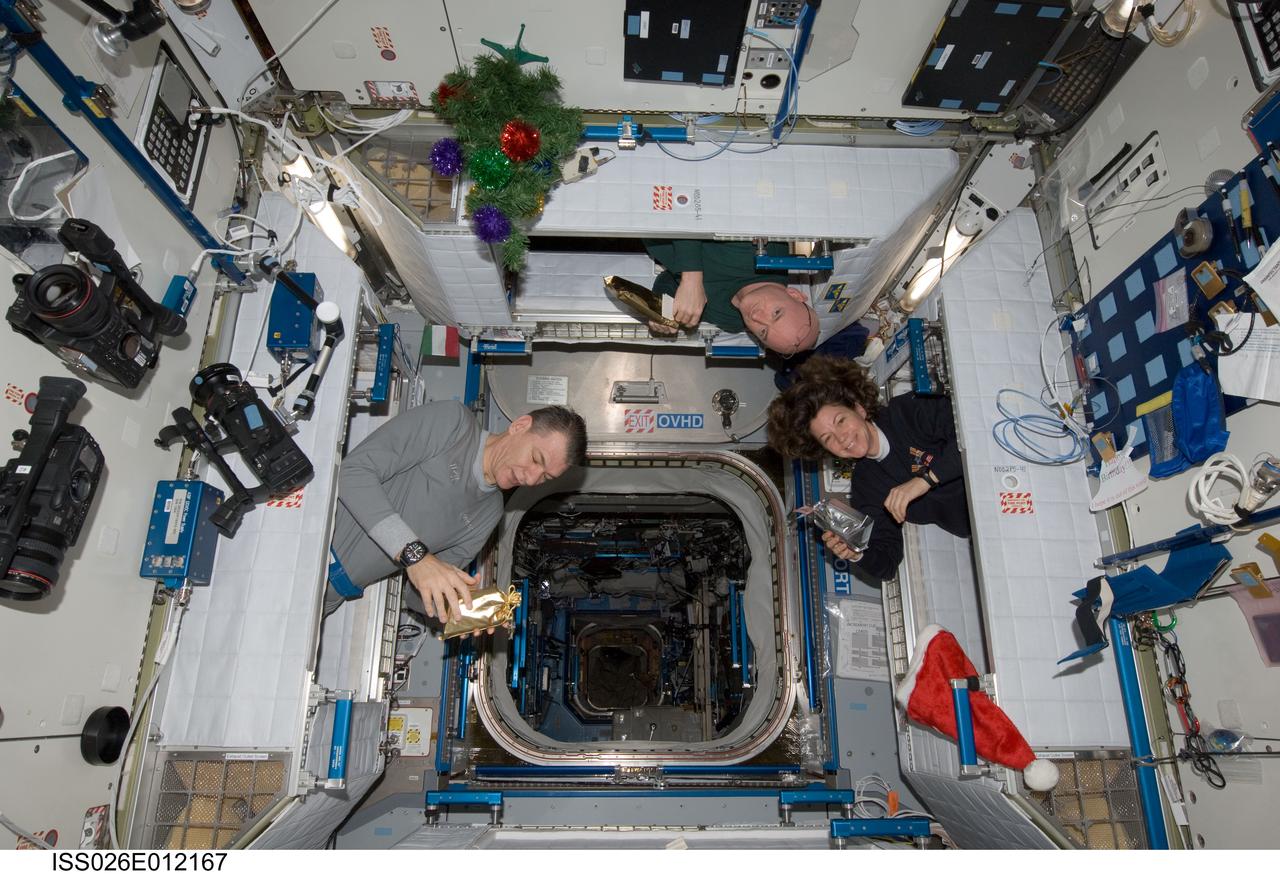 ISS026-E-012167 (25 Dec. 2010) --- Three of the six crew members aboard the International Space Station peek out of their sleeping quarters on Christmas morning to view the station’s decorations and gifts. Shown, from left, are European Space Agency astronaut Paolo Nespoli, Expedition 26 flight engineer, NASA astronaut Scott Kelly, Expedition 26 commander, and NASA astronaut Catherine (Cady) Coleman, flight engineer