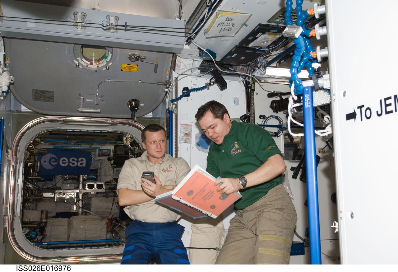 ISS026-E-016976 (11 Jan. 2011) --- Russian cosmonauts Dmitry Kondratyev (left) and Oleg Skripochka, both Expedition 26 flight engineers, look over a procedures manual during an emergency scenarios drill in the Harmony node of the International Space Station.