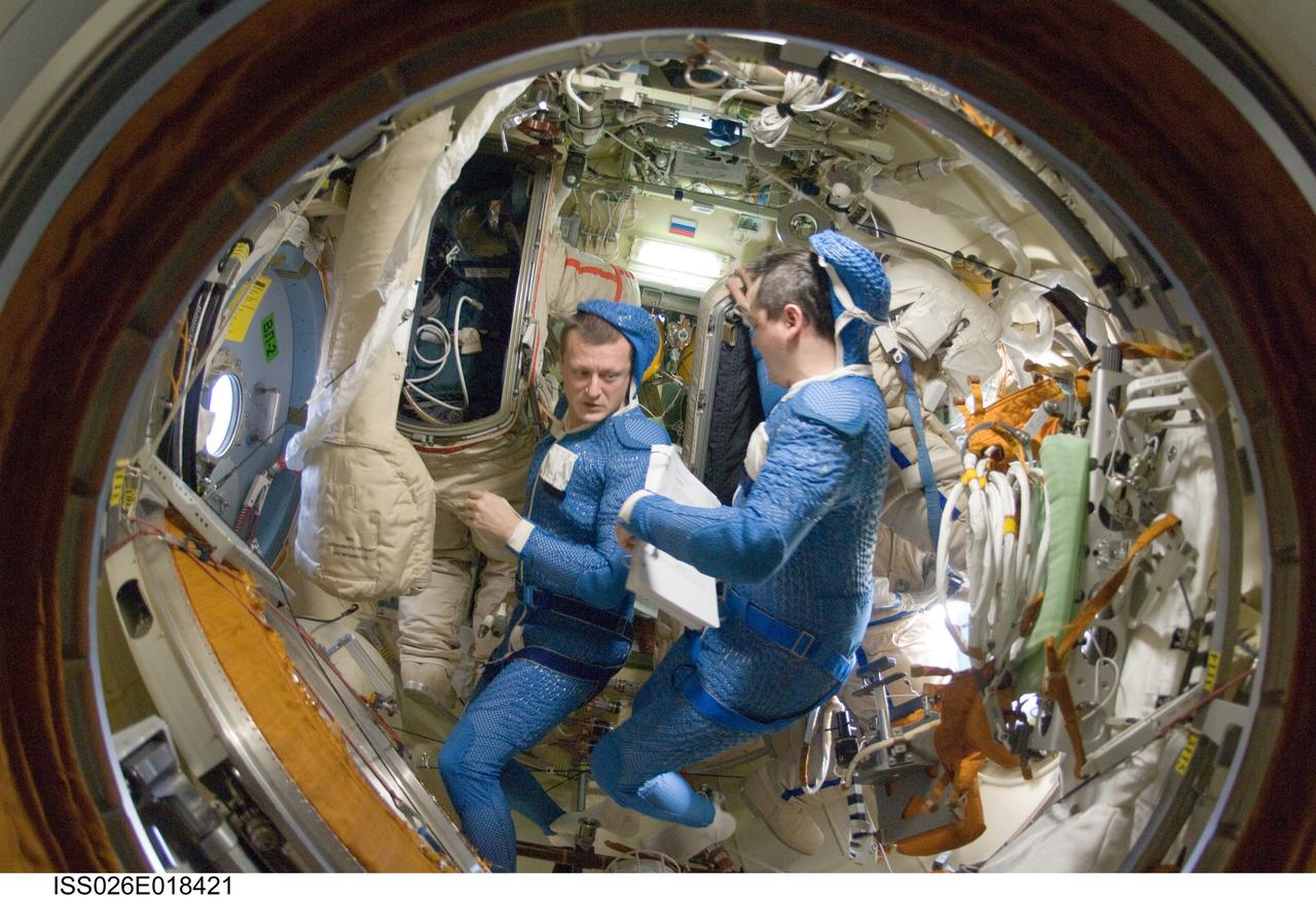 ISS026-E-018421 (18 Jan. 2011) --- Attired in blue thermal undergarments that complement the Russian Orlan spacesuit, Russian cosmonauts Dmitry Kondratyev (left) and Oleg Skripochka, both Expedition 26 flight engineers, prepare to don and check out their Orlan spacesuits in preparation for a spacewalk scheduled for Jan. 21, 2011. During the spacewalk Kondratyev and Skripochka will complete the installation of a new high-speed data transmission system, remove an old plasma pulse experiment, install a camera for the new Rassvet docking module and retrieve a materials exposure package.