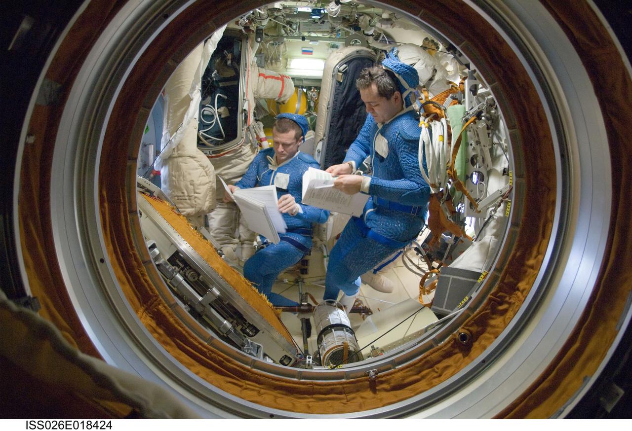 ISS026-E-018424 (18 Jan. 2011) --- Attired in blue thermal undergarments that complement the Russian Orlan spacesuit, Russian cosmonauts Dmitry Kondratyev (left) and Oleg Skripochka, both Expedition 26 flight engineers, prepare to don and check out their Orlan spacesuits in preparation for a spacewalk scheduled for Jan. 21, 2011. During the spacewalk Kondratyev and Skripochka will complete the installation of a new high-speed data transmission system, remove an old plasma pulse experiment, install a camera for the new Rassvet docking module and retrieve a materials exposure package.