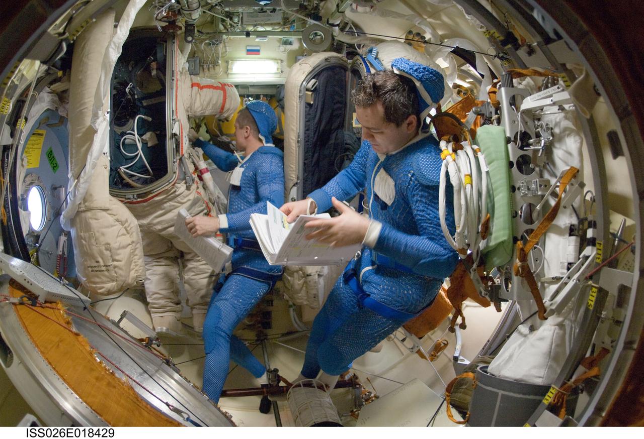 ISS026-E-018429 (18 Jan. 2011) --- Attired in blue thermal undergarments that complement the Russian Orlan spacesuit, Russian cosmonauts Dmitry Kondratyev (left) and Oleg Skripochka, both Expedition 26 flight engineers, prepare to don and check out their Orlan spacesuits in preparation for a spacewalk scheduled for Jan. 21, 2011. During the spacewalk Kondratyev and Skripochka will complete the installation of a new high-speed data transmission system, remove an old plasma pulse experiment, install a camera for the new Rassvet docking module and retrieve a materials exposure package.