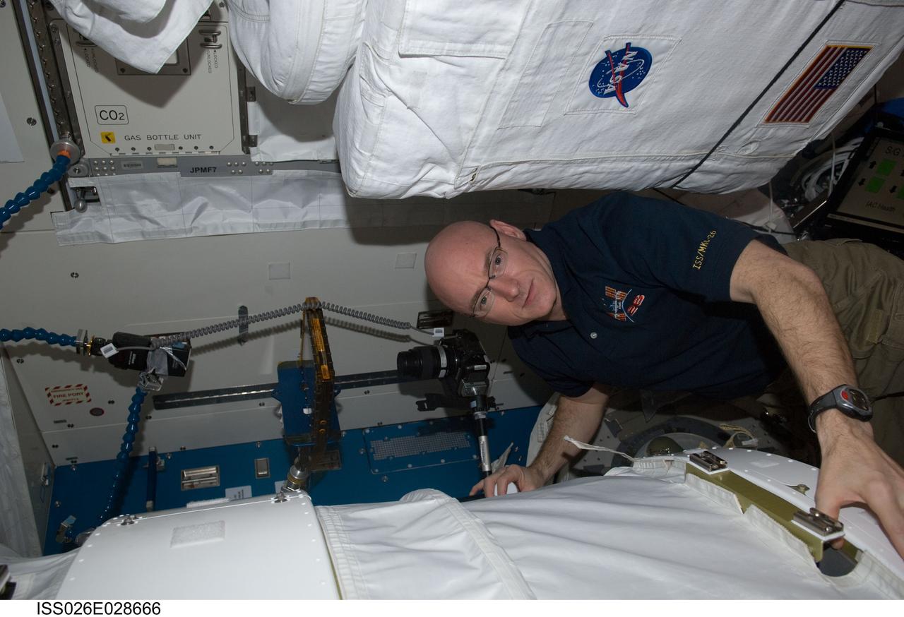 ISS026-E-028666 (23 Feb. 2011) --- NASA astronaut Scott Kelly, Expedition 26 commander, uses a digital still camera to photograph the Binary Colloidal Alloy Test-5 (BCAT-5) payload setup in the Kibo laboratory of the International Space Station.