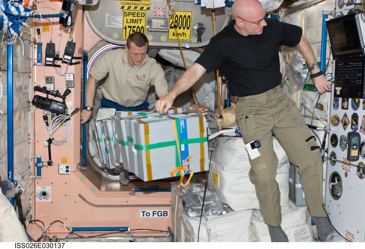 ISS026-E-030137 (25 Feb. 2011) --- NASA astronaut Scott Kelly (foreground), Expedition 26 commander; and Russian cosmonaut Dmitry Kondratyev, flight engineer, move stowage containers in the Unity node of the International Space Station.