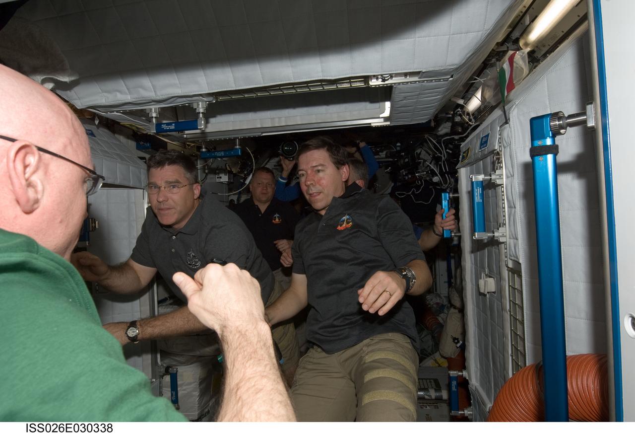 ISS026-E-030338 (26 Feb. 2011) --- STS-133 and Expedition 26 crew members are pictured shortly after space shuttle Discovery and the International Space Station docked in space and the hatches were opened. Pictured are NASA astronauts Scott Kelly (left foreground), Expedition 26 commander; Steve Bowen (left) and Michael Barratt (right foreground), both STS-133 mission specialists. Visible in the background are NASA astronauts Eric Boe (left), STS-133 pilot; and Steve Lindsey (mostly obscured at right), STS-133 commander.