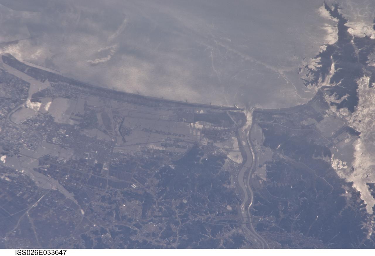ISS026-E-033647 (13 March 2011 --- From 220 miles above Japan, an Expedition 26 crew member onboard the International Space Station took this 800mm view of the coast northeast of Sendai, between Matsushima Bay and the port of Ishinomake, on March 13. Sunglint helps to highlight the flood waters over the land, flowing out the rivers, plus oils swirling on the surface with the currents.