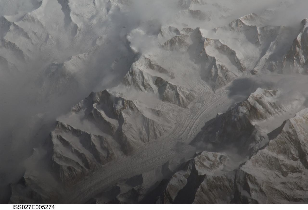 ISS027-E-005274 (16 March 2011) --- Central Tien Shan in the People?s Republic of China is featured in this image photographed by an Expedition 27 crew member on the International Space Station (ISS). The Tien Shan (or ?celestial mountains? in Chinese) is one of the largest continuous mountain ranges in the world, extending approximately 2,500 kilometers roughly east-west across Central Asia. This photograph provides a detailed view of part of the central Tien Shan, located approximately 64 kilometers east of a point where the borders of China, Kyrgyzstan, and Kazakhstan meet. While the image looks like it might have been taken from an airplane, it was taken from the space station at an altitude of 341 kilometers. The distance between the ISS ground track position (approximately 304 kilometers to the southwest) and the imaged area produces an oblique ? looking outwards an angle, rather than straight down ? view that, together with shadowing of valleys, accentuates the mountainous topography. Like the Himalayas to the south, the uplift of the Tien Shan results from the ongoing collision between the Eurasian and Indian continental tectonic plates. The rugged topography of the range is the result of subsequent erosion by water, wind, and in the highest parts of the range, active glaciers. Two types of glaciers are visible in the image; cirque glaciers occupy amphitheater-like depressions on the upper slopes of the mountains, and feed ice downslope to aggregate into large valley glaciers such as the one visible at center. Low clouds obscure an adjacent valley and glaciers to the north (upper left). Two high peaks of the central Tien Shan are identifiable in the image. Xuelian Feng has a high summit of 6,527 meters above sea level. To the east, the aptly-named Peak 6231 has summit of 6,231 meters above sea level.