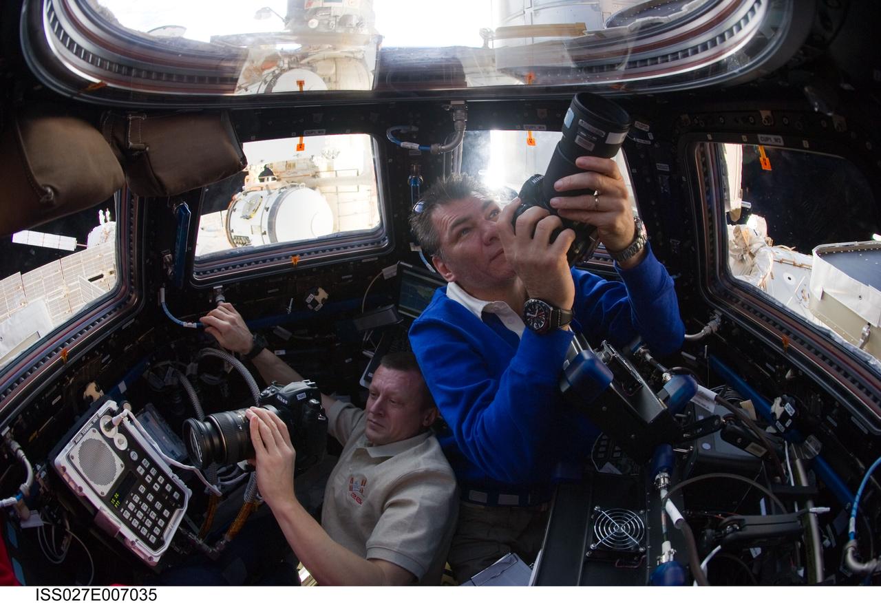 ISS027-E-007035 (19 March 2011) --- Russian cosmonaut Dmitry Kondratyev (left), Expedition 27 commander; and European Space Agency astronaut Paolo Nespoli, flight engineer, use still cameras at windows in the Cupola of the International Space Station.