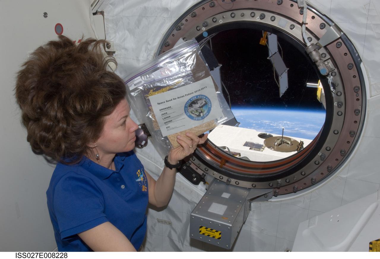 ISS027-E-008228 (26 March 2011) --- NASA astronaut Cady Coleman, Expedition 27 flight engineer, holds a bag of space seeds near a window in the Kibo laboratory of the International Space Station.