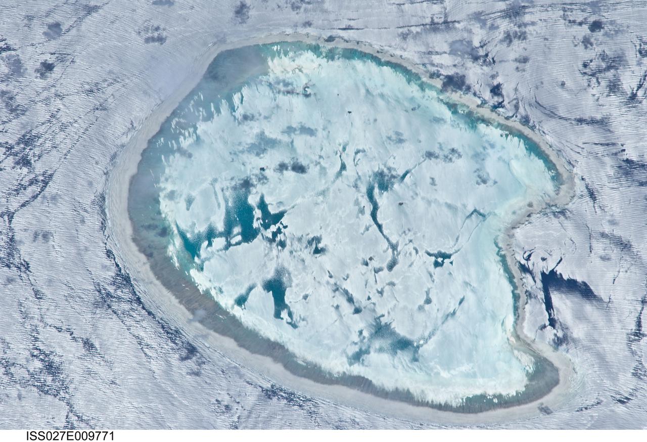 ISS027-E-009771 (2 April 2011) --- Bassas da India is featured in this image photographed by an Expedition 27 crew member on the International Space Station. The vantage point of crew members onboard the space station provides many dramatic views of Earth?s surface. This detailed photograph of the Bassas da India, an uninhabited atoll in the Indian Ocean (between the Mozambique coast of Africa and the island of Madagascar) has an almost surreal quality due to varying degrees of sunglint. Sunglint is an optical phenomena caused by light reflecting off of a water surface directly back towards the observer. Variations in the roughness of the water surface?presence or absence of waves due to wind and water currents?will cause differences in the intensity of the sunglint. The presence of other materials, such as oils or surfactants, can also change the properties of the water surface. Here the presence of currents is highlighted as darker patches or streaks (left and upper right). In contrast, shallow water in the lagoon (center) presents a more uniform, mirror-like appearance in sunglint suggesting that there are no subsurface currents present. Wave crests visible around the atoll are likely the result of both surface winds and subsurface currents. The Bassas da India atoll is part of the French Southern and Antarctic Lands. It is uninhabited due to its complete submergence during high tide ? there is no vegetation established on the atoll for the same reason. The atoll is approximately 10 kilometers in diameter, and covers an area (including the lagoon) of approximately 80 square kilometers.