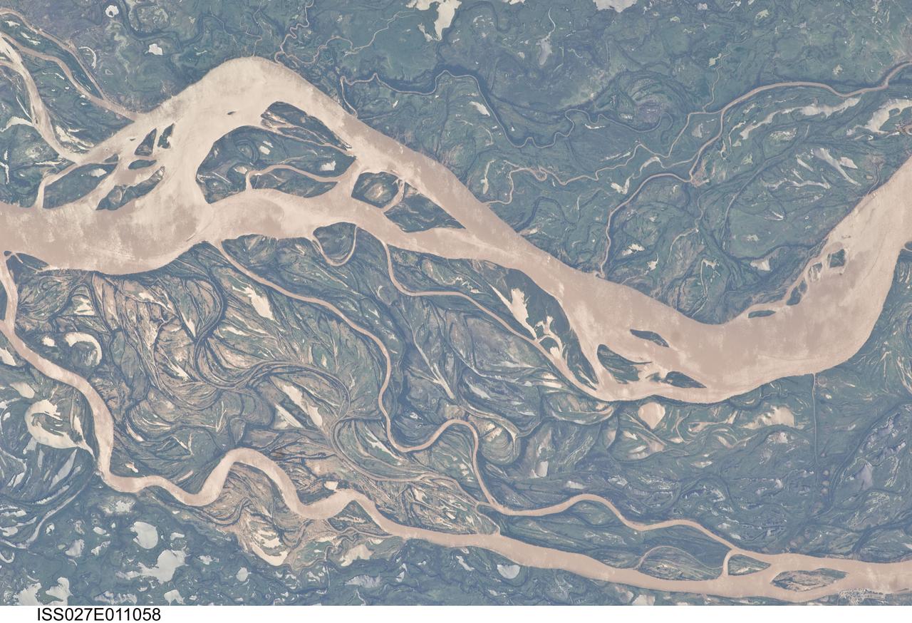ISS027-E-011058 (9 April 2011) --- The Parana River floodplain in northern Argentina is featured in this image photographed by an Expedition 27 crew member on the International Space Station. This image shows a 29-kilometer stretch of the Parana River, South America?s second largest river, downstream of the small city of Goya (barely distinguishable as grayer surfaces in the extreme top left corner of the image). The Parana River ranges up to three kilometers wide along the reach illustrated in the image. Its strong brown color indicates that it is carrying a heavy load of muddy sediment. Smaller active side channels also carry this muddy water. Numerous lakes are typical on active floodplains, and appear here as irregular bodies of water. Some appear brown, indicating that they have been refilled during recent higher flood levels of the active channels. The main channel Parana River (top) is deep enough to allow smaller ocean-going ships to pass north of the illustrated region to the capital city of Asuncion in landlocked Paraguay, fully 1,200 kilometers inland (well out of the image). The Parana River is thus an important transportation route for landlocked cities such as Asuncion and inland cities of eastern landlocked Bolivia and inland Brazil. The Parana floodplain occupies the entire image; it is so wide?18 kilometers?that its banks are not visible. Numerous curved, or meandering past channels are the most prominent characteristic of the floodplain. These indicate prior positions of rivers. As river beds move laterally by natural processes, they leave remnants of their channels, which appear as lakes, and finally fill with mud. This is an excellent image for illustrating these meander forms. From a geological standpoint it is interesting that almost all the past channels are similar in curvature to the smaller active side rivers; almost no forms show, in any obvious way, prior positions of the main, very wide Parana channel. The reverse might be expected since the main channel is so dominant in the modern landscape.