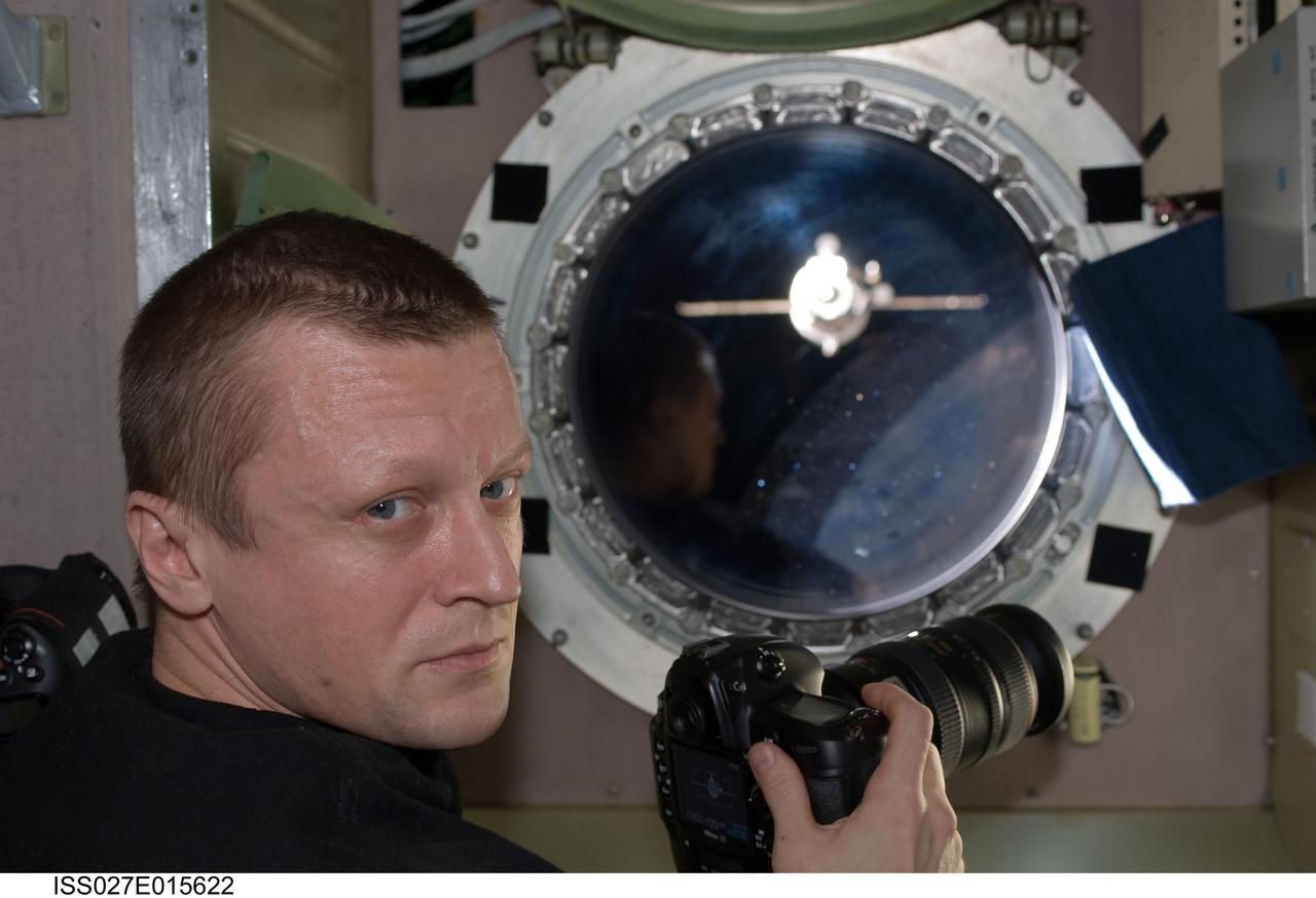 ISS027-E-015622 (22 April 2011) --- Russian cosmonaut Dmitry Kondratyev, Expedition 27 commander, is pictured near a window in the Zvezda Service Module of the International Space Station while photographing the departure of the unpiloted ISS Progress 41 supply vehicle.