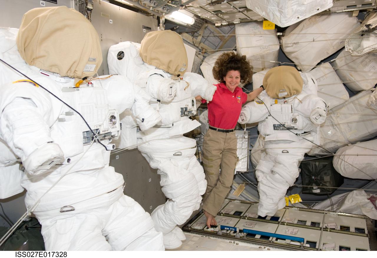 ISS027-E-017328 (27 April 2011) --- NASA astronaut Cady Coleman, Expedition 27 flight engineer, poses with three Extravehicular Mobility Unit (EMU) spacesuits in the Permanent Multipurpose Module (PMM) of the International Space Station.