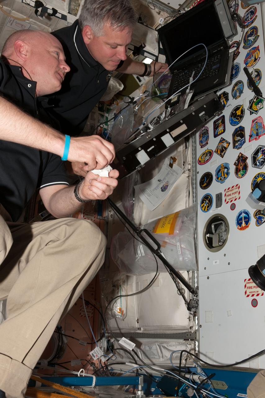 ISS027-E-035420 (21 May 2011) --- NASA astronaut Mark Kelly, Expedition 27 commander, looks at the various mission insignias placed in the Unity node of the International Space Station before placing the STS-134 insignia among them. NASA astronaut Greg H. Johnson, pilot, is pictured as well.