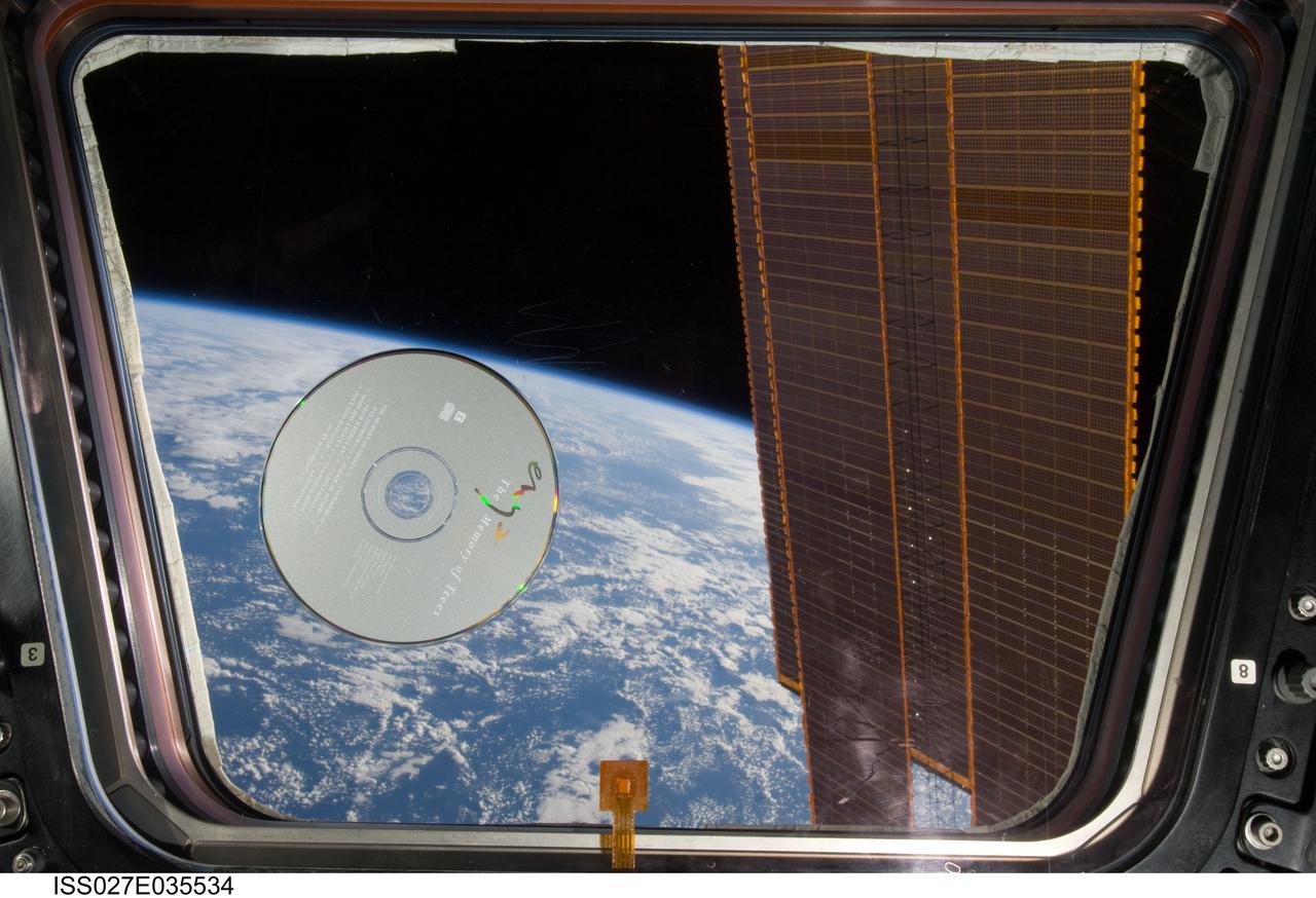 View of a music CD, The Memory Of Trees by Enya, floating in front of a window in the Cupola Module during Expedition 27 / STS-134 joint operations.