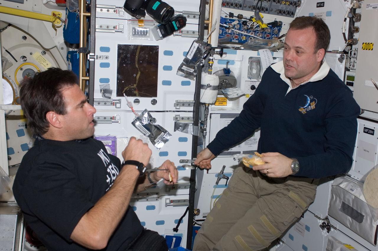 ISS028-E-005140 (24 May 2011) --- NASA astronauts Greg Chamitoff (left), STS-134 mission specialist; and Ron Garan, Expedition 28 flight engineer, discuss mission activities while enjoying a snack on the middeck of space shuttle Endeavour while docked with the International Space Station.