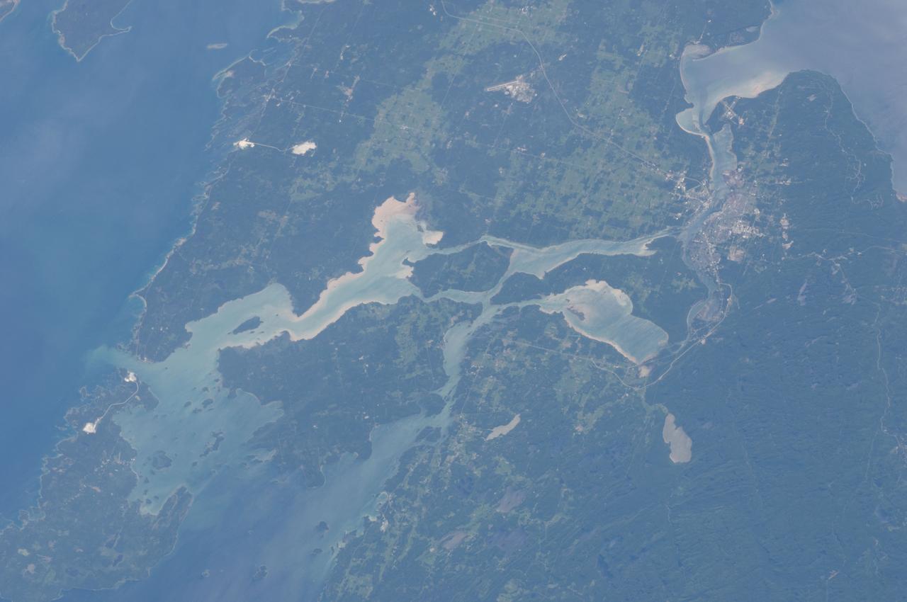 ISS028-E-010162 (29 June 2011) --- Sault Ste Marie, Ontario and Michigan are featured in this image photographed by an Expedition 28 crew member on the International Space Station. The twin cities of Sault Ste Marie are located across the St. Mary?s River that forms part of the international boundary between Canada (Province of Ontario) and the United States (State of Michigan). This photograph highlights the two cities, together with the region of lakes and islands that separates Lakes Huron and Superior, two of the Great Lakes of North America. Smaller lakes include Lake George to the west; the large forested islands of St. Joseph and Drummond are visible at lower left. The Sault Ste Marie urban areas (upper right) have a distinctive gray to white coloration in the image, contrasting with the deep green of forested areas in Ontario and the lighter green of agricultural fields in Michigan. The coloration of water surfaces in the lakes and rivers varies from blue to blue-green to silver, and is likely caused by varying degrees of sediment and sunglint ? light reflecting back to the observer on the space station from the water surface, much as light reflects from a mirror. Prior to formalization of the US/Canada border in 1817, Sault Ste Marie was a single community. Archeological evidence suggests that the region had been occupied by Native Americans at least five hundred years ago. A mission ? the first European settlement in Michigan ? was established there in 1668 by the French Jesuit Father Jacques Marquette. Today, shipping locks and canals in both urban areas are an important part of the Great Lakes shipping traffic system.