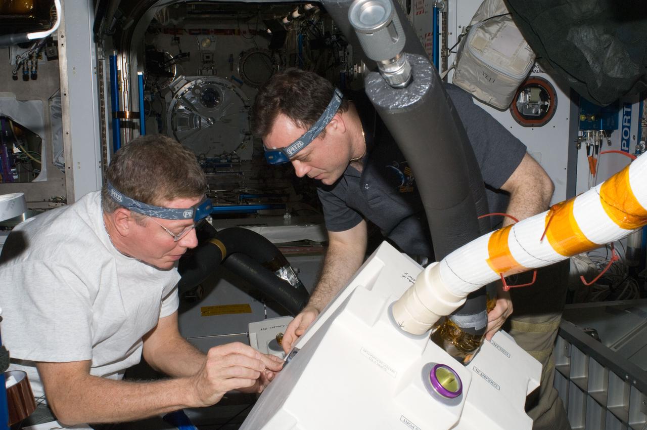 ISS028-E-010781 (30 June 2011) --- NASA astronauts Mike Fossum (left) and Ron Garan, both Expedition 28 flight engineers, perform in-flight maintenance in the Harmony node of the International Space Station. The maintenance involved removing and replacing the failed Common Cabin Air Assembly (CCAA) heat exchanger in the P3 Midbay with a new spare Heat Exchanger Orbit Replaceable Unit (HX ORU) and lines.