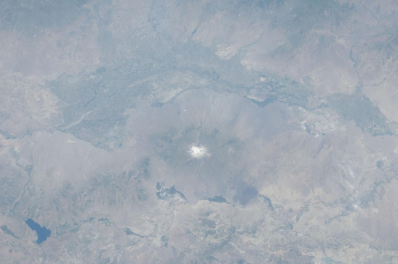 ISS028-E-015023 (8 July 2011) --- The Aras River and Turkey-Armenia-Iran border region are featured in this image photographed by an Expedition 28 crew member on the International Space Station. This photograph highlights a segment of the international border between Turkey to the south-southwest and Armenia to the north-northeast. The Aras River is the physical expression of the closed border between the two countries. Extensive green agricultural fields are common on both sides of the river (top), as well as a number of gray to tan urban areas including Artashat and Armavir in Armenia and Igdir in Turkey. While there have been efforts to normalize diplomatic relations between the two countries in recent years, the Armenia-Turkey border remains officially closed. The dominant geographic feature in the region is Mt. Ararat, also known as Agri Dagi. The peak of Ararat, a large stratovolcano that last erupted in 1840 according to historical records, is located approximately 40 kilometers to the south of the Armenia-Turkey border. A lower peak to the east, known as Lesser or Little Ararat, is also volcanic in origin. Dark gray lava flows to the south of Mt. Ararat are located near the Turkish border with Iran. While this border is also closed along much of its length, official crossing points allow relatively easy travel between the two countries. The white, glacier-clad peak of Mt. Ararat is evident at center; dark green areas on the lower slopes indicate where vegetation cover is abundant. A large lake, Balik Golu or Fish Lake, is visible to the west (lower left).