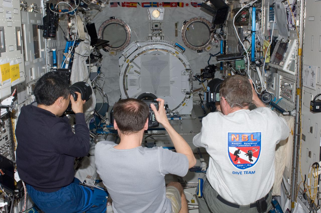ISS028-E-015033 (9 July 2011) --- Japan Aerospace Exploration Agency astronaut Satoshi Furukawa (left), Russian cosmonaut Sergei Volkov (center) and NASA astronaut Mike Fossum, all Expedition 28 flight engineers, use still cameras in the International Space Station’s Kibo laboratory to photograph a detailed outline of the orbiter’s underbelly. The space shuttle “pattern” was traditionally used as a training tool by the station crew members preparing for the R-Bar Pitch Maneuver performed by each arriving shuttle. The image size represents the orbiter at a distance of about 600 feet on approach. During an RPM, typically more than 300 images are taken using cameras outfitted with 400, 800 and 1000 mm lenses and downlinked to the ground for analysis to clear the Thermal Protection System for entry.