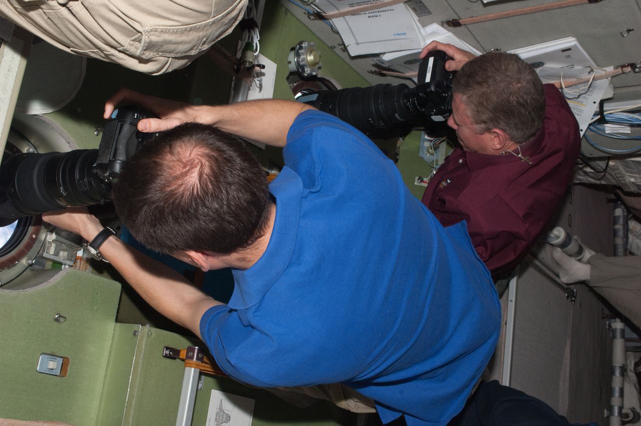 ISS028-E-015803 (10 July 2011) --- Russian cosmonaut Sergei Volkov, Expedition 28 flight engineer, aims a camera through a window on the Zvezda service module to record the space shuttle Atlantis during rendezvous operations on July 12, 2011. Crewmate and fellow flight engineer Mike Fossum, NASA astronaut, is seen at right.