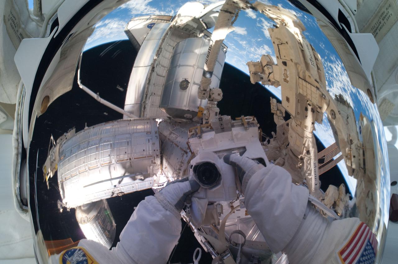 ISS028-E-016173 (12 July 2011) --- Because of his shiny helmet visor, this "self portrait" of NASA astronaut Mike Fossum, photographed during a July 12 spacewalk, mirrors a panoramic scene of the docked International Space Station and space shuttle Atlantis and the blue and white Earth below.