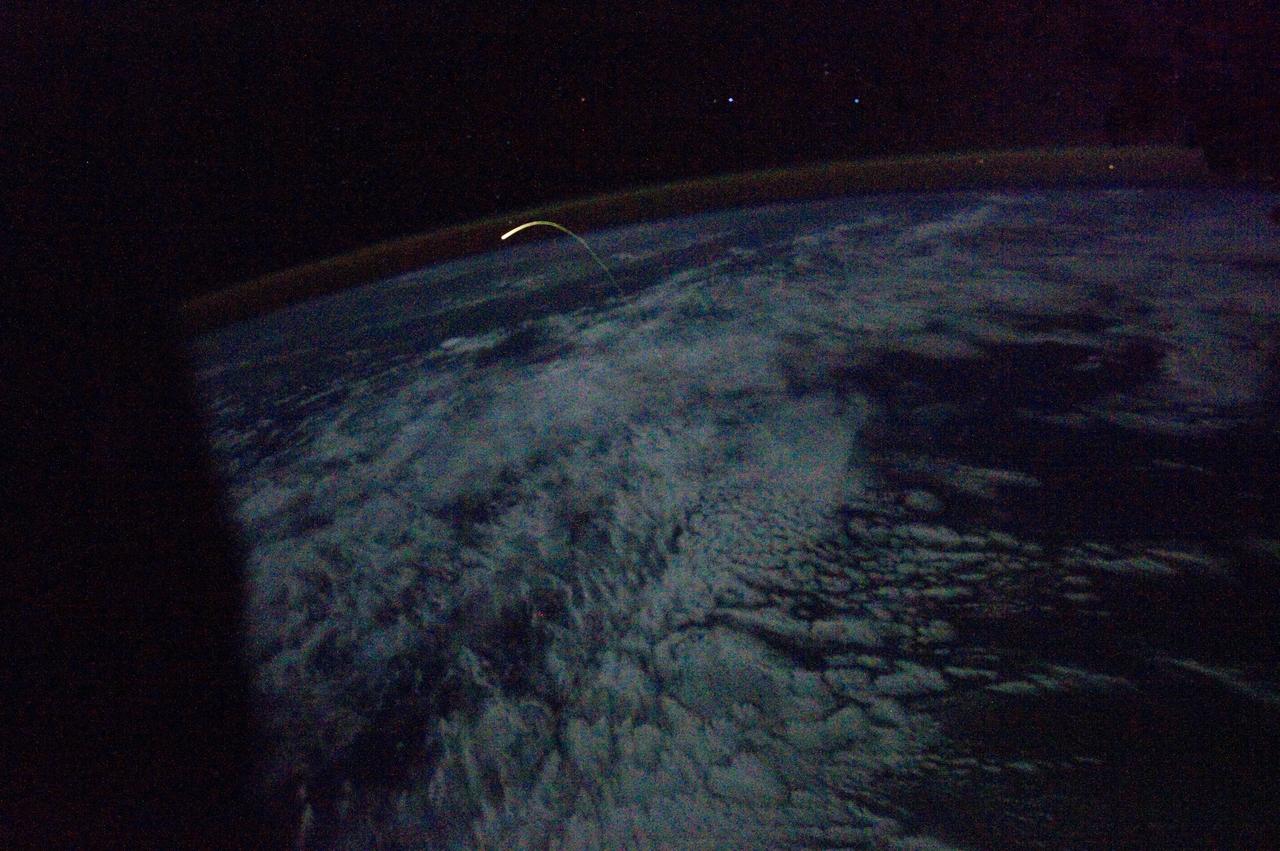 ISS028-E-018216 (21 July 2011) --- This unprecedented view of the space shuttle Atlantis, appearing like a bean sprout against the darkness of space, a faint line of airglow over a dark cloud-covered Earth, on its way home, was photographed by the crew of the International Space Station. Airglow over Earth can be seen in the background.