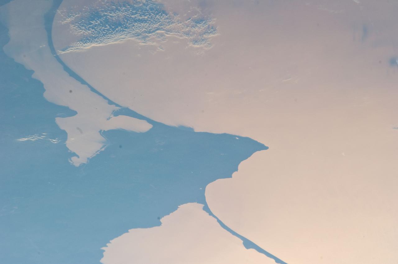 ISS028-E-024146 (2 Aug. 2011) --- Kaliningrad and Baltic Sea, Russia are featured in this image photographed by an Expedition 28 crew member on the International Space Station. This striking photograph reveals detail of the two great lagoons to the north and south of Kaliningrad, each protected from the open waters of the Baltic Sea by the thin perfect curves of current-generated sand spits. A broad arm of agricultural country separates the freshwater lagoons?known as Kurshsky Bay (or the Curonian Lagoon further north in Lithuania, just outside the top of the image) and the Vistula Lagoon. From the crew member perspective in low Earth orbit, land surfaces usually appear brighter than water, which normally appears darker and often black. Reflected sunlight, or sunglint, inverts this pattern. The reflected light in this image is a pink or coppery hue, indicating the likely existence of smog in the air since smog particles enhance the red part of the light spectrum. Camera settings used to acquire sunglint images result in high contrast that reveals excellent detail of coastlines and surface features of waterbodies, but masks land surface detail. The thin, 50 kilometer-long barge canal leading from the Baltic Sea to Kaliningrad is visible but the great port of Kaliningrad itself is not. Other human patterns on this intensively developed landscape such as towns, highways and farm boundaries are likewise masked in the image. The area has a long human history. The growth of the Vistula spit finally cut off the north Polish city of Elblag (just outside the bottom of the image) from the Baltic Sea in the 13th century. To reconnect Elblag directly with the Baltic Sea, the EU is considering funding the digging of another canal through the spit at lower right, despite ecological concerns. Kaliningrad was heavily damaged during WWII and then annexed by Russia and cleared of its German population. As the only Russian port on the Baltic Sea to be ice-free year-round, Kaliningrad then gained importance strategically as home of the Baltic Fleet.