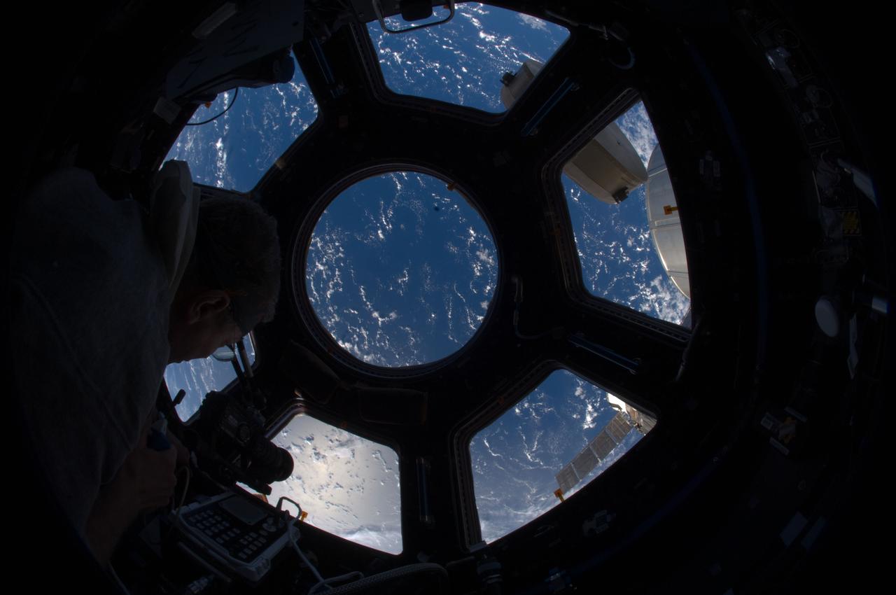 ISS028-E-028791 (22 Aug. 2011) --- NASA astronaut Mike Fossum, Expedition 28 flight engineer, uses a camera at a window in the Cupola of the International Space Station. A blue and white part of Earth is visible through the windows.