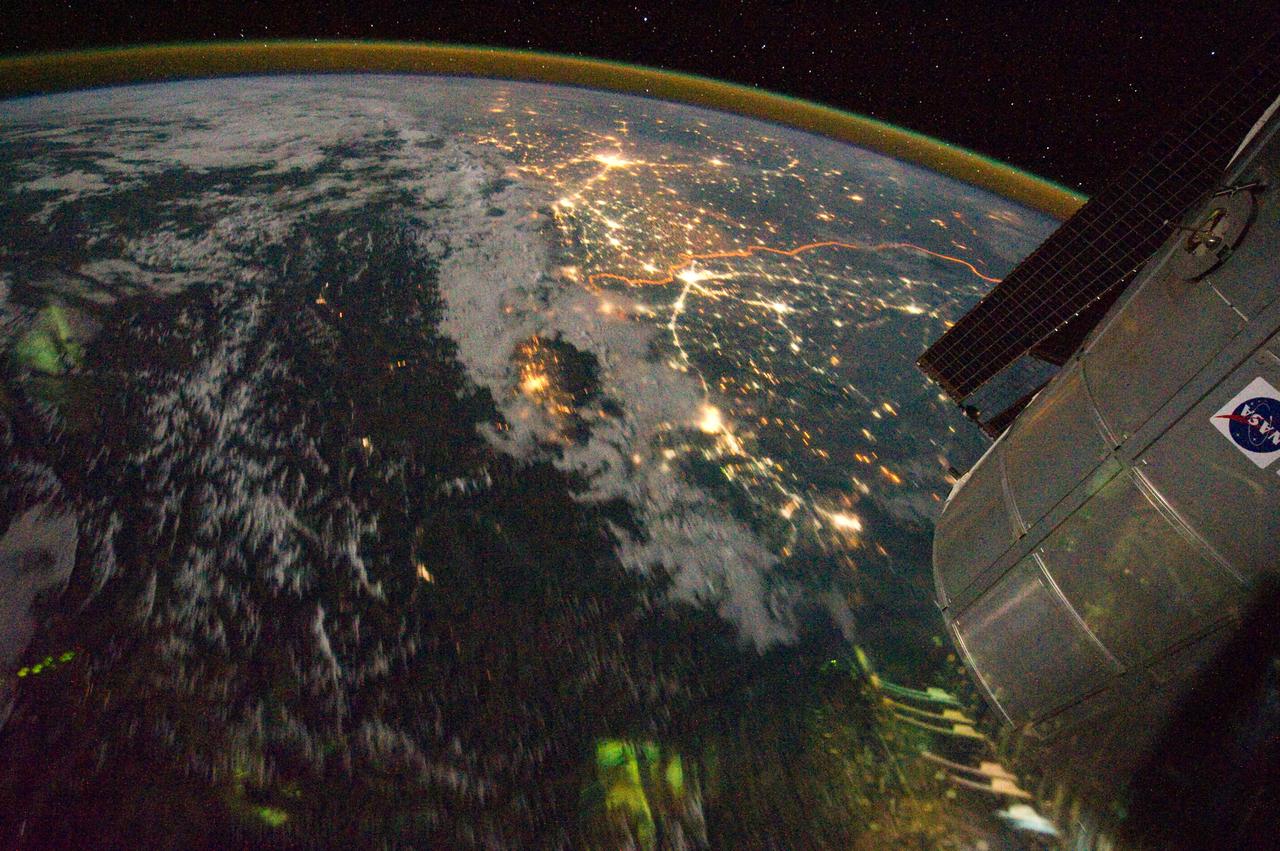 ISS028-E-029679 (21 Aug. 2011) --- A night time view of India-Pakistan borderlands is featured in this image photographed by an Expedition 28 crew member on the International Space Station. Clusters of yellow lights on the Indo-Gangetic Plain of northern India and northern Pakistan reveal numerous cities both large and small in this photograph. Of the hundreds of clusters, the largest are the metropolitan areas associated with the capital cities of Islamabad, Pakistan in the foreground and New Delhi, India at the top?for scale these metropolitan areas are approximately 700 kilometers apart. The lines of major highways connecting the larger cities also stand out. More subtle but still visible at night are the general outlines of the towering and partly cloud-covered Himalayan ranges immediately to the north (left). A striking feature of this photograph is the line of lights, with a distinctly more orange hue, snaking across the central part of the image. It appears to be more continuous and brighter than most highways in the view. This is the fenced and floodlit border zone between the countries of India and Pakistan. The fence is designed to discourage smuggling and arms trafficking between the two countries. A similar fenced zone separates India?s eastern border from Bangladesh (not visible). This image was taken with a 16-mm lens, which provides the wide field of view, as the space station was tracking towards the southeast across the subcontinent of India. The station crew took the image as part of a continuous series of frames, each frame taken with a one-second exposure time to maximize light collection ? unfortunately, this also causes blurring of some ground features. The distinct, bright zone above the horizon (visible at top) is produced by airglow, a phenomena caused by excitation of atoms and molecules high in the atmosphere (above 80 kilometers, or 50 miles altitude) by ultraviolet radiation from the sun. Part of the ISS Permanent Multipurpose Module, or PMM, and a solar panel array are visible at right.