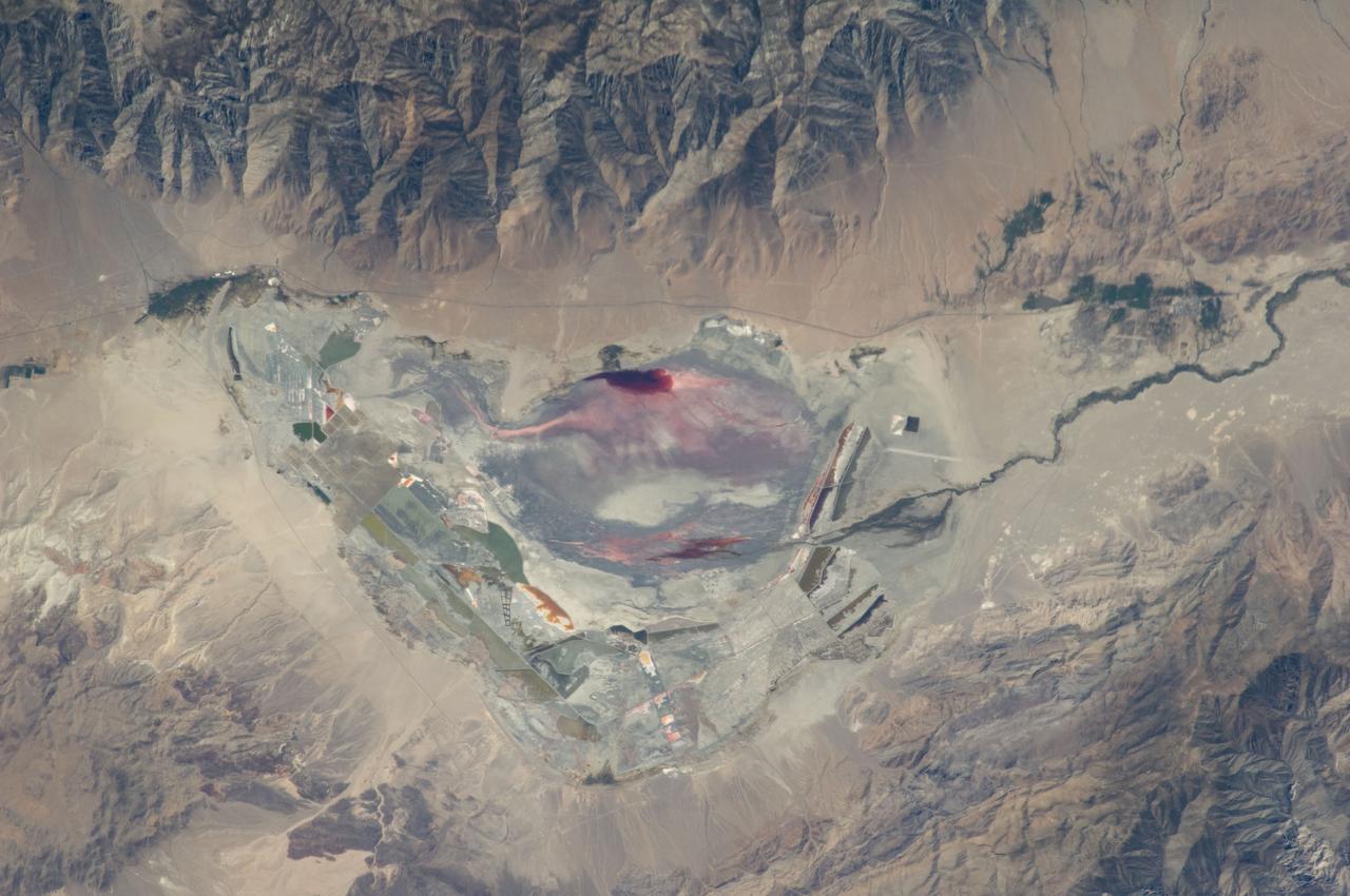 ISS028-E-035137 (30 Aug. 2011) --- Owens Lake in California is featured in this image photographed by an Expedition 28 crew member on the International Space Station. This photograph highlights the mostly dry bed of Owens Lake, located in the Owens River Valley between the Inyo Mountains and the Sierra Nevada. Shallow groundwater, springs, and seeps support minor wetlands and a central brine pool. Two bright red areas along the margins of the brine pool indicate the presence of halophilic, or salt-loving organisms known as Achaeans. Grey and white materials within the lake bed are exposed lakebed sediments and salt crusts. The towns of Olancha and Lone Pine are delineated by the presence of green vegetation indicating a more constant availability of water. According to scientists, the present-day Owens Lake was part of a much larger lake and river system that existed during the Pleistocene Epoch (approximately 3 million to approximately 12,000 years ago) along the current northeastern border of California with Nevada. Meltwater from alpine glaciers in the Sierra Nevada filled the regional valleys of the Basin and Range to form several glacial lakes that were ancestral to the now-dry lakebeds (or playas) of Owens, Searles Lake, and China Lake. While Searles and China Lakes dried out due to regional changes to a hotter and drier climate over thousands of years, Owens Lake became desiccated largely due to the diversion of Owens River water in the early 20th century to serve the needs of the City of Los Angeles, CA located 266 kilometers to the south. Following complete desiccation of the lakebed in 1926, significant amounts of windblown dust were produced ? indeed, the term ?Keeler fog? was coined by residents of the now largely abandoned town on the eastern side of Owens Lake due to the dust. In addition to adverse health effects on local residents, dust from Owens Lake has been linked to visibility reduction in nearby national parks, forests, and wilderness areas. Recently, efforts to control dust evolution from the lakebed have been undertaken by the City of Los Angeles.
