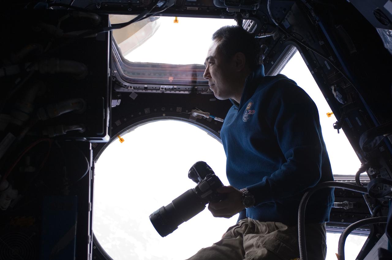 ISS029-E-033716 (30 Oct. 2011) --- Japan Aerospace Exploration Agency astronaut Satoshi Furukawa, Expedition 29 flight engineer, holds a still camera while looking through a window in the Cupola of the International Space Station Space Station.