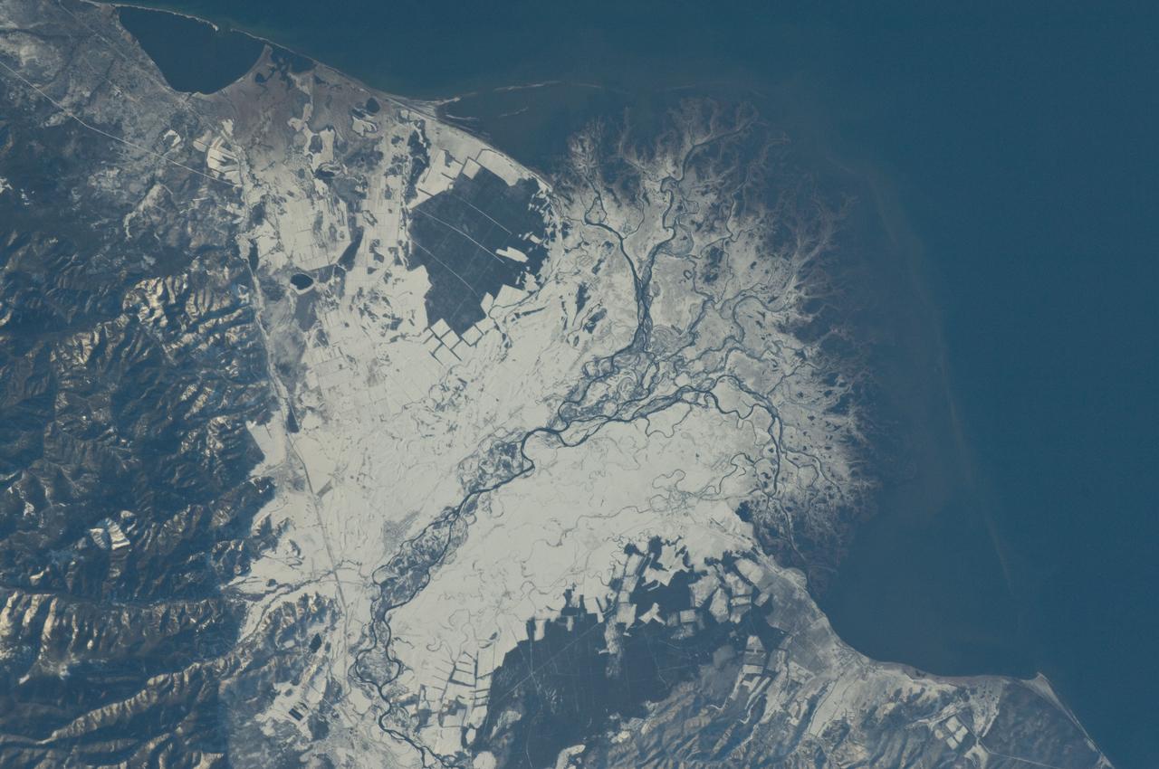 ISS029-E-037915 (3 Nov. 2011) --- Snowfall on the Selenga River Delta, Russian Federation is featured in this image photographed by an Expedition 29 crew member on the International Space Station. This photograph illustrates the Selenga River Delta built out into Lake Baikal in Russia. The Selenga River delta (center) is lobate in form, with an intricate network of distributary channels and levees surrounded by marshlands building out into Lake Baikal. This suggests that development of the delta is governed by the sediment load carried by the river, and any modifications of form due to lake tides or waves are relatively minor. Further out, dark brown depositional bars are visible forming a rough arc marking the edge of the delta. Snow cover on the river floodplain highlights numerous secondary channels, as well as channels previously occupied by the river but now abandoned. The regular outlines of agricultural fields to the southwest and northeast of the river are also highlighted by the snow cover. Lake Baikal is a World Heritage Site. The Selenga River is the major contributor of water to Lake Baikal; it occupies approximately 82 per cent of the watershed area for the lake. The wetlands of the Selenga River delta are designated as a RAMSAR site and provide valuable habitat for more than 170 species of birds, including many that are migrating. Like Baikal, the Selenga Delta is home to unique ecosystems, including more than 70 rare or endangered species of plants and animals. Waters of the Selenga River serve many (and differing) uses in both Mongolia and Russia, including support of agriculture, provision of drinking water, light industry, mining, recreation, and tourism. These uses also contribute to degradation of the river water quality, downstream availability of water, and ecological impacts. For example, a pulp and paper plant in the city of Selenginsk (lower left) has been tied to high levels of pollution in the river. International efforts to integrate management of the Selenga River basin for both ecological and economic sustainability are ongoing.