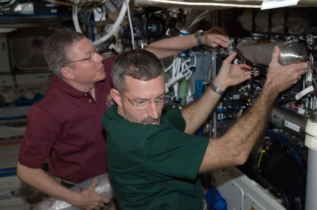 ISS029-E-043263 (19 Nov. 2011) --- NASA astronauts Mike Fossum (left), Expedition 29 commander; and Dan Burbank, flight engineer, remove and replace Combustion Integrated Rack (CIR) manifold bottles in the Destiny laboratory of the International Space Station.