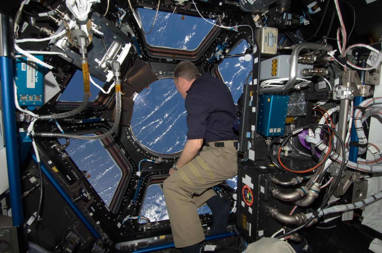 ISS029-E-043397 (19 Nov. 2011) --- NASA astronaut Mike Fossum, Expedition 29 commander, looks through a window in the Cupola of the International Space Station. A blue and white part of Earth is visible through the windows.