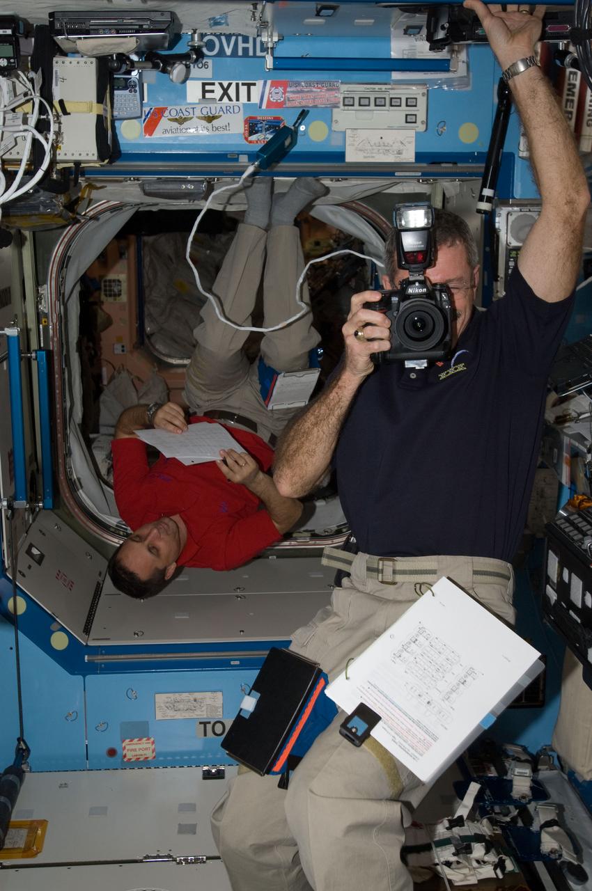 ISS030-E-007556 (3 Dec. 2011) --- NASA astronaut Dan Burbank (foreground), Expedition 30 commander, uses a still camera while Russian cosmonaut Anton Shkaplerov, flight engineer, reads a procedures checklist in the Destiny laboratory of the International Space Station.