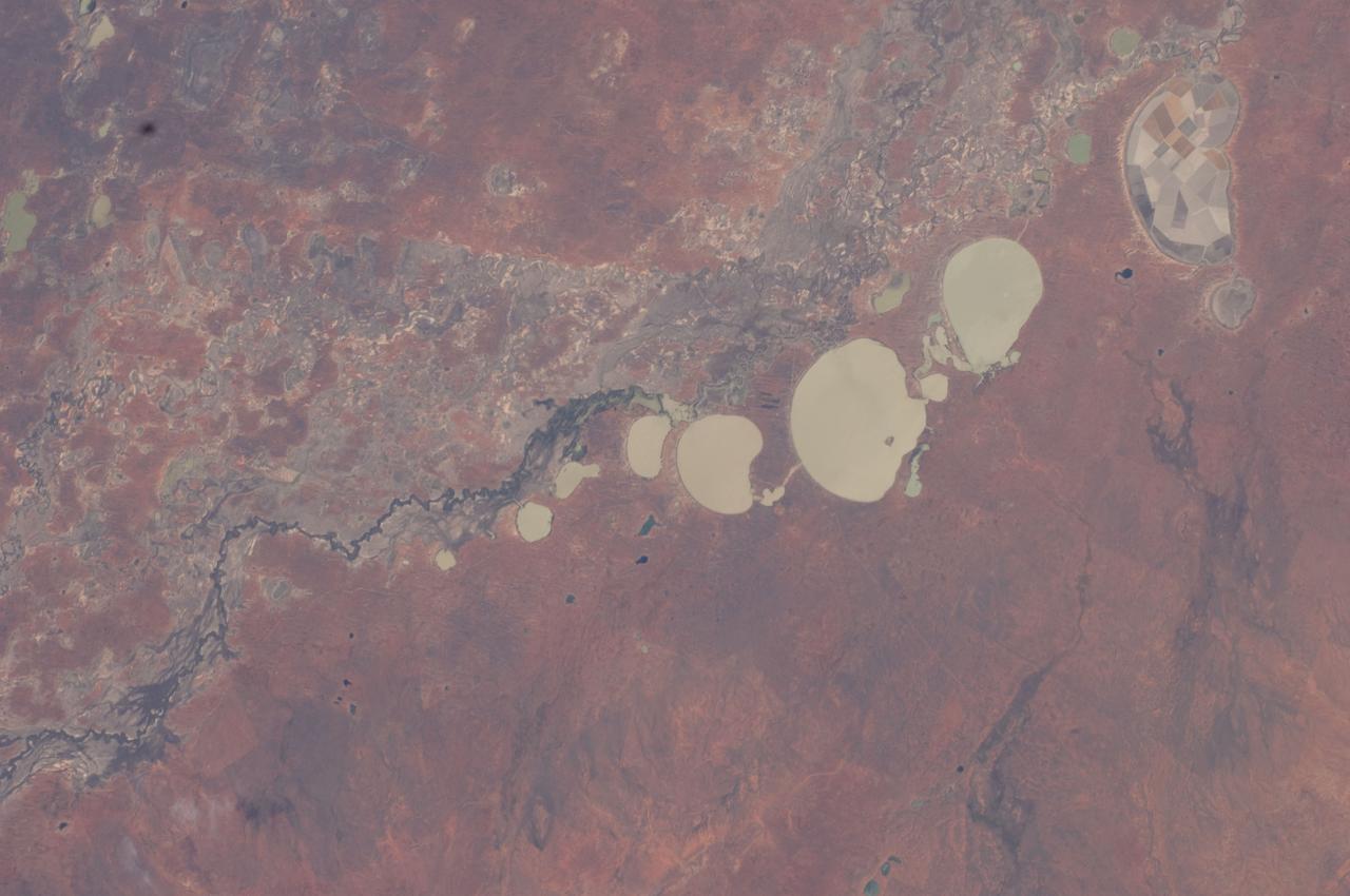 ISS030-E-009186 (3 Dec. 2011) --- The Menindee Lakes, New South Wales, Australia are featured in this image photographed by an Expedition 30 crew member on the International Space Station. The Menindee Lakes comprise a system of ephemeral, freshwater lakes fed by the Darling River when it floods. The lakes lie in the far west of New South Wales, Australia, near the town of Menindee. The longest is Lake Tandou (18.6 kilometers north?south dimension), visible at the upper right of this photograph. The lakes appear to have a small amount of water flooding them. The Darling River itself was flowing, as indicated by the dark water and blackened mud along its course (left). The Darling River flows southwest in tortuous fashion (bottom left to upper right). In the flat landscapes of this part of Australia, the river has created several inland deltas in its course to the sea, with characteristic diverging channel patterns, marked by younger sediments, which appear grayer than the surrounding ancient red soils and rocks. One such inland delta appears at right where minor channels wind across the countryside. The apex of another inland delta appears at upper right. Some of the Menindee Lakes have been incorporated in an artificially regulated overflow system providing for flood control, water storage for domestic use and livestock, as well as downstream irrigation. The lakes are also important as wetlands supporting a rich diversity of birds. The floor of one lake, Lake Tandou, is also used as prime agricultural land, as can be seen by its patchwork of irrigated fields, and is protected from flooding.
