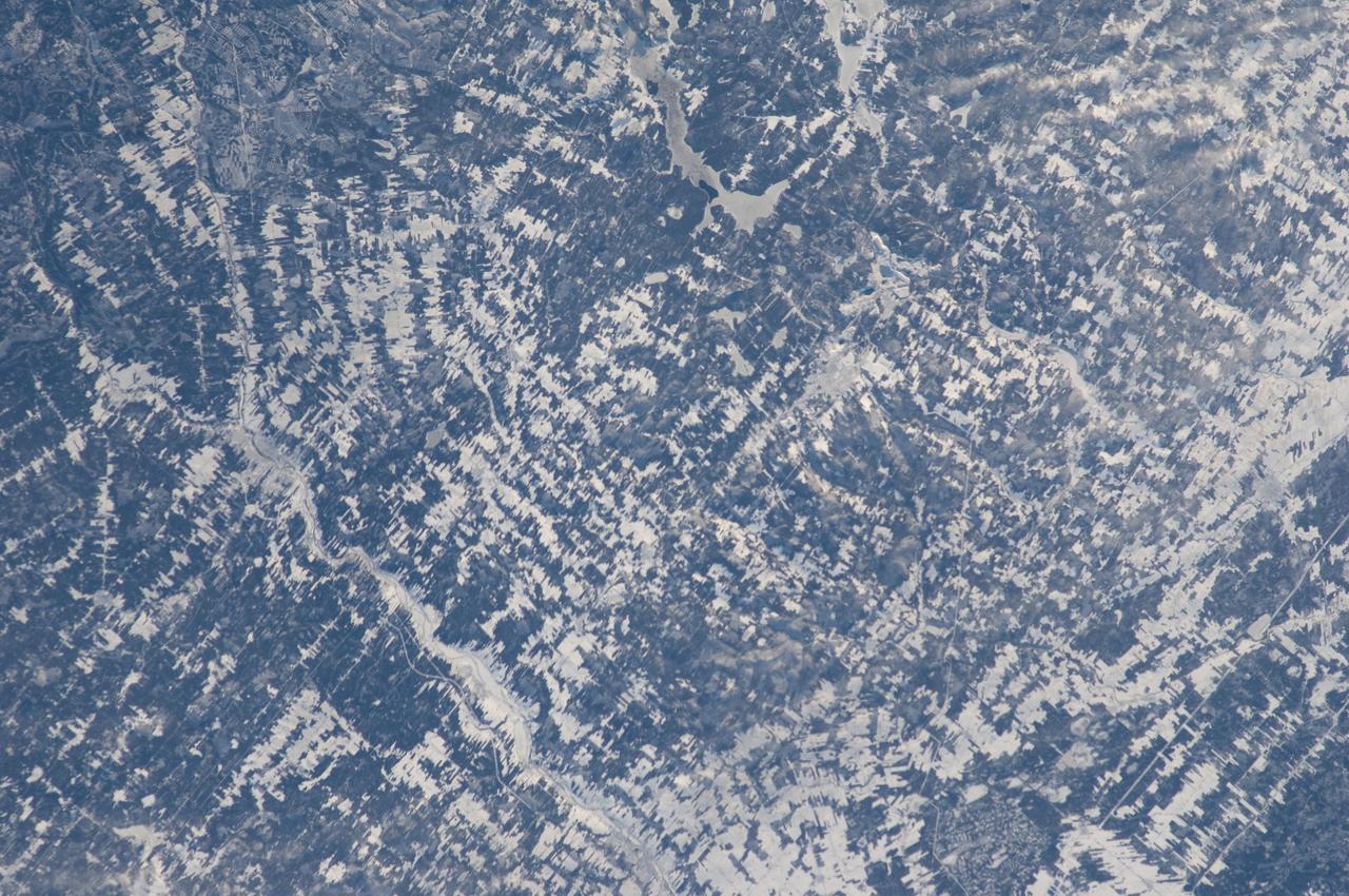 ISS030-E-019144 (29 Dec. 2011) --- Agricultural patterns in Quebec, Canada are featured in this image photographed by an Expedition 30 crew member on the International Space Station. The region shown in the image, known as the Chaudiere-Appalaches, is located midway between Quebec City (the provincial capital) and the international border with the United States (specifically, the State of Maine). Agriculture is a significant component of Quebec’s industries, with over 50 per cent of the food produced or processed consumed within the province as of 2008 (source: Agriculture and Agri-Food Canada). The tapestry-like pattern is due to the fact that the agricultural fields in the region are closely tied to access roads, with rectangular fields extending outwards perpendicular to the roadways. A similar pattern—embedded within a different social, historical, and economic context—can be seen in the Rondonia region of western Brazil. Snow cover highlights the rectangular fields interspersed with dark green forested patches. The urban area of Saint Georges (left) is visible as a light gray region along the Chaudiere River. The Parc national de Frontenac borders parts of Lac (lake) St.-Francois at upper center, providing an area for outdoor recreation within the intensive agricultural landscape.