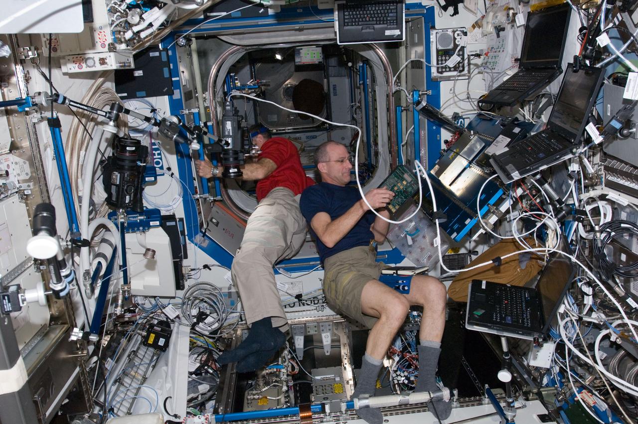ISS030-E-022574 (28 Dec. 2011) --  NASA astronaut Don Pettit (foreground),Expedition 30 flight engineer, performs the Enhanced Processor and Integrated Communications (EPIC) card testing and X2R10 software transition.  The software transition work will include EPIC card testing and card installations, and monitoring of the upgraded Multiplexer/ Demultiplexer (MDM) computers.  Dan Burbank, Expedition 30 commander, is setting up a camcorder in the background.