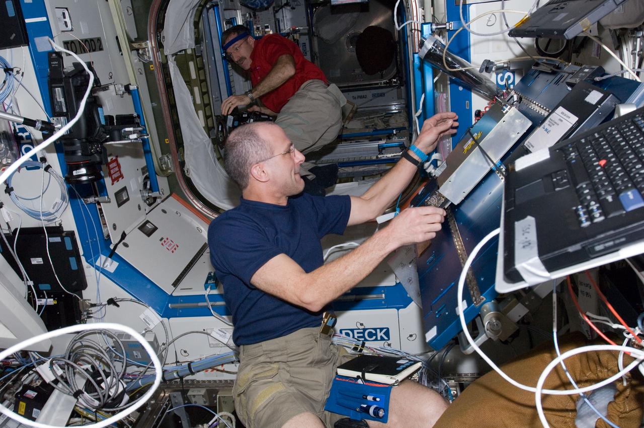 ISS030-E-022575 (28 Dec. 2011) --  NASA astronaut Don Pettit (foreground),Expedition 30 flight engineer, performs the Enhanced Processor and Integrated Communications (EPIC) card testing and X2R10 software transition.  The software transition work will include EPIC card testing and card installations, and monitoring of the upgraded Multiplexer/ Demultiplexer (MDM) computers.  Dan Burbank, Expedition 30 commander, is setting up a camcorder in the background.