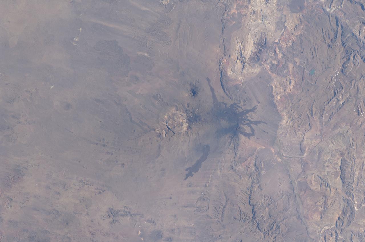 ISS030-E-030265 (31 Dec. 2011) --- The Payun Matru Volcanic Field in Argentina is featured in this image photographed by an Expedition 30 crew member on the International Space Station. The Payun Matru (3,680 meters above sea level) and Payun Liso (3,715 meters above sea level) stratovolcanoes are the highest points of the Payun Matru Volcanic Field located in west-central Argentina, approximately 140 kilometers to the east of the Andes mountain chain. This photograph illustrates some of the striking geological features of the field visible from space. The summit of Payun Matru is dominated by a roughly 15 kilometer-in-diameter caldera (center), formed by an explosive eruption sometime after approximately 168,000 years ago. Several dark lava flows, erupted from smaller vents and fissures, are visible in the northwestern part of the volcanic field. One distinct flow, erupted from Volcan Santa Maria located to the northwest of Payun Matru, is approximately 15 kilometers long. A number of small cinder cones, appearing as brown dots due to the short lens used, are built on older lava flows (grey) to the northeast of Payun Matru. While there is no recorded historical observation of the most recent volcanic activity in the field, oral histories suggest that activity was witnessed by indigenous peoples. Most Andean volcanoes—and earthquakes—follow the trend of the greater Andes chain of mountains, and are aligned roughly N-S above the tectonic boundary between the subducting (descending) Nazca Plate and the overriding South American Plate as is predicted from plate tectonic theory. Other major volcanic centers located some distance away from the major trend typically result from more complex geological processes associated with the subduction zone, and can provide additional insight into the subduction process.