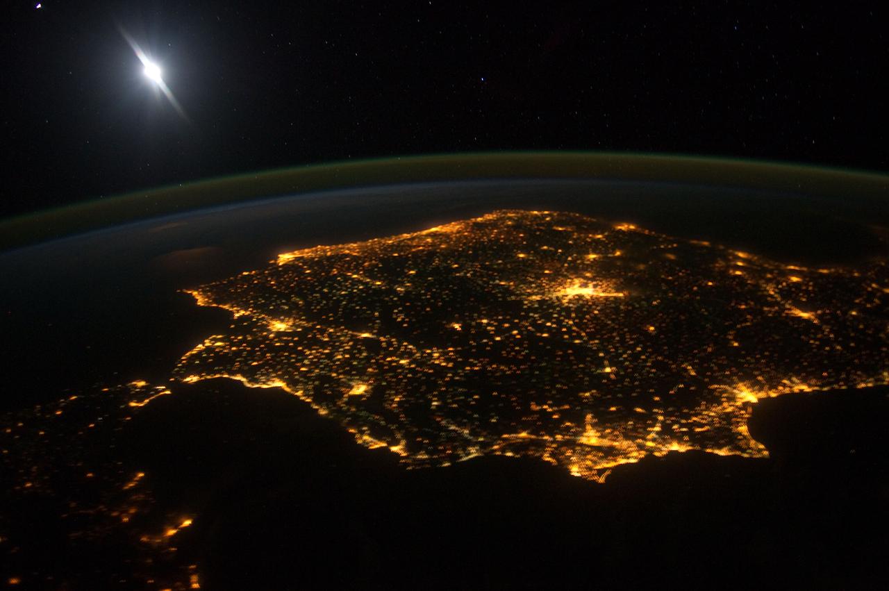 ISS030-E-060478 (30 Jan. 2012) --- The city lights of Madrid (just right of center) stand out in this photograph from the International Space Station. Recorded by one of the Expedition 30 crew members, the view shows almost the entire Iberian Peninsula (both Spain and Portugal) with the Strait of Gibraltar and Morocco appearing at lower left. What is thought to be a blur of the moon appears in upper left corner. The faint gold or brownish line of airglow?caused by ultraviolet radiation exciting the gas molecules in the upper atmosphere?parallels the horizon or Earth limb.