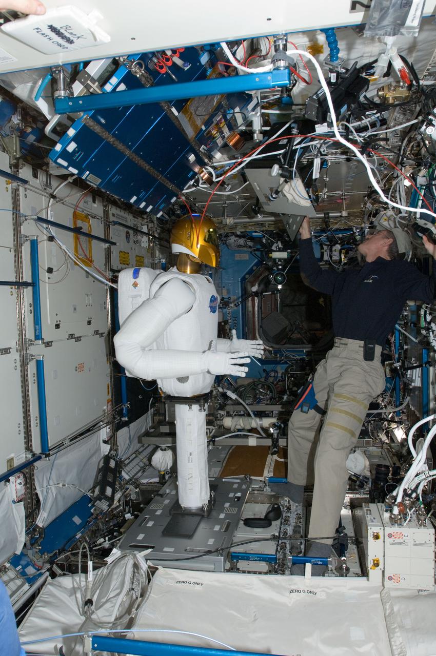 ISS030-E-074062 (15 Feb. 2012) --- Robonaut 2, nicknamed R2, is pictured in the Destiny laboratory of the International Space Station while NASA astronaut Dan Burbank, Expedition 30 commander, uses a computer during R2?s initial checkouts.